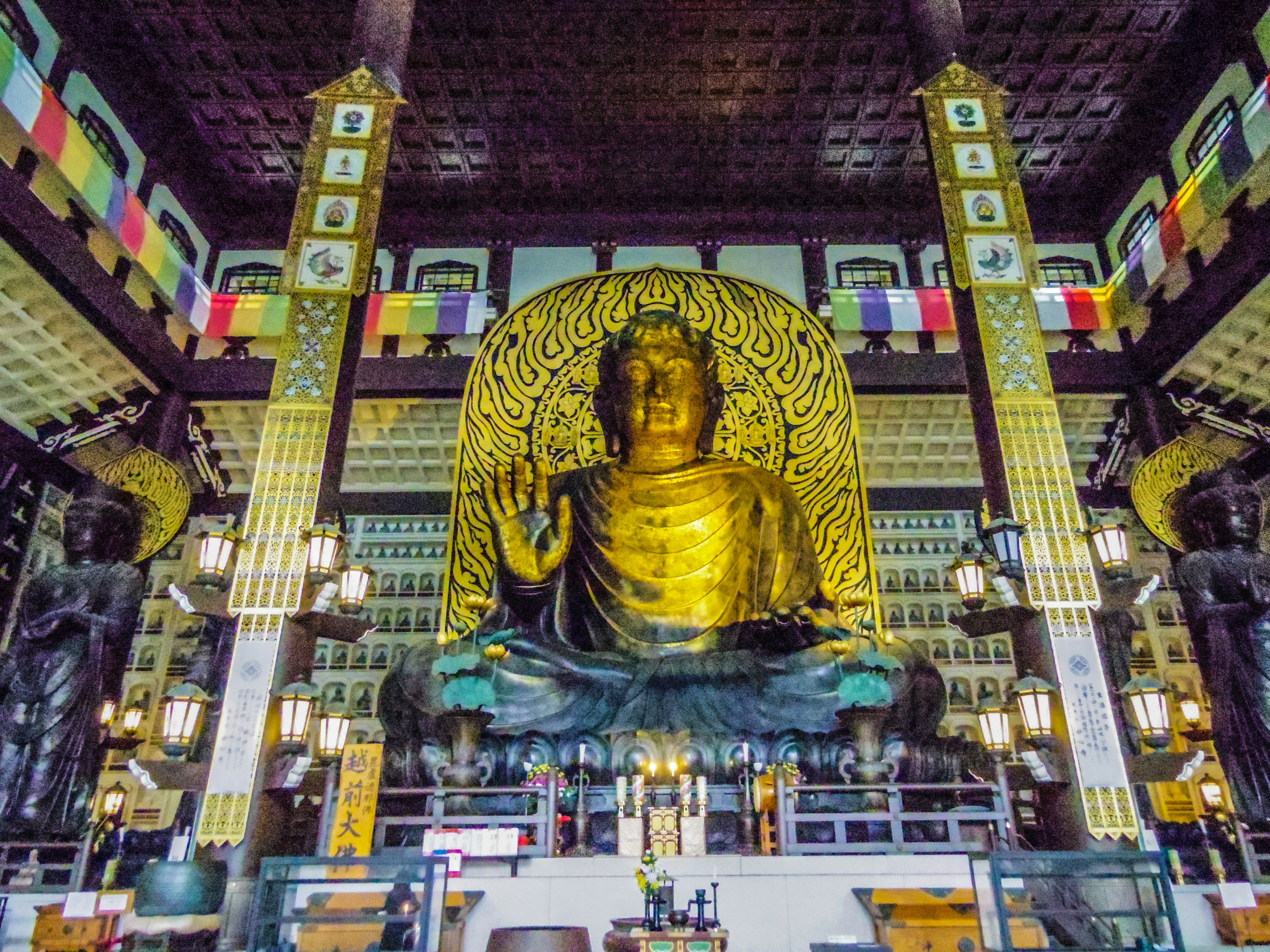 Interior of a temple featuring a large golden Buddha statue surrounded by colorful decorations and lights