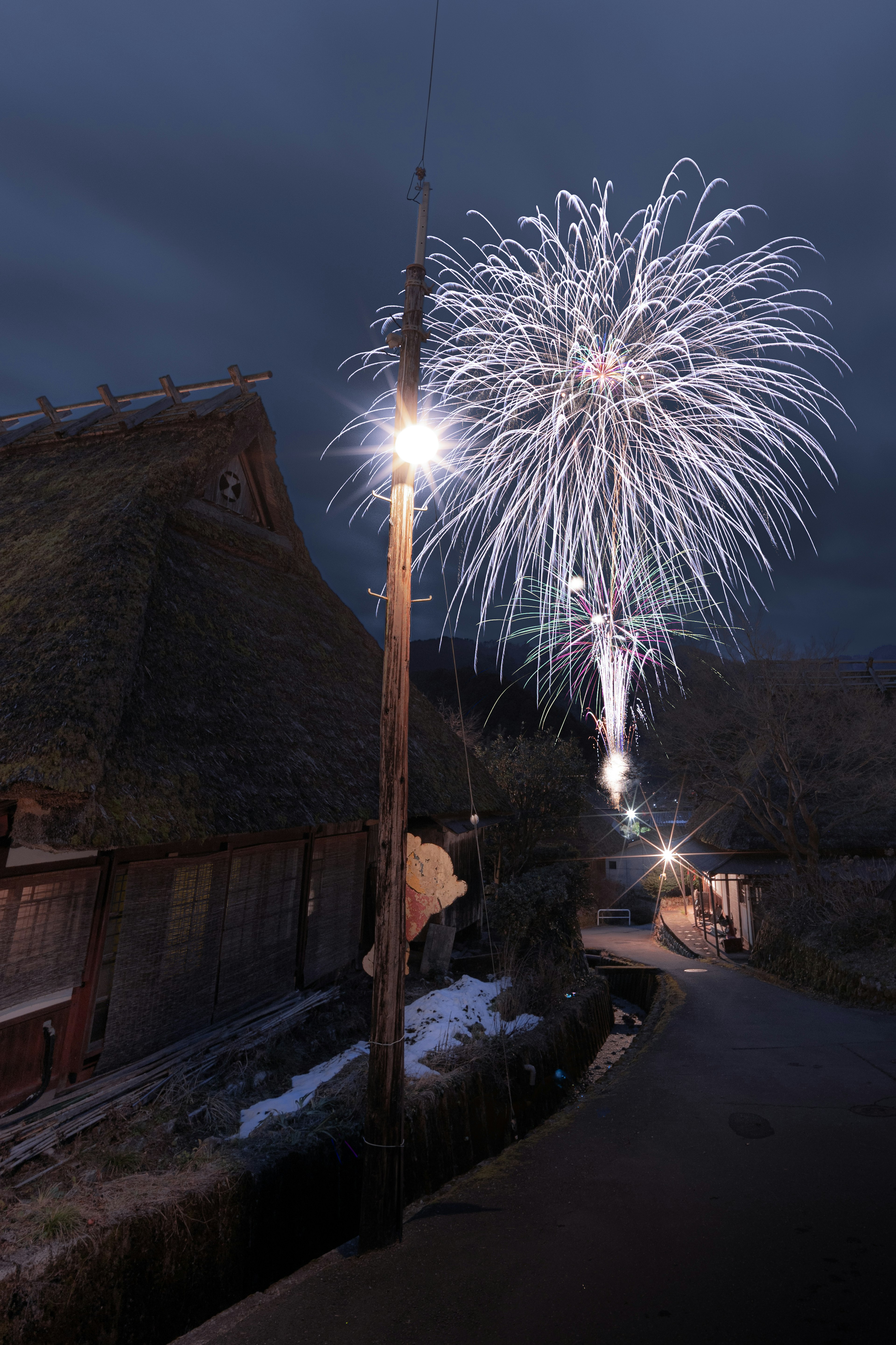 Scena notturna invernale con fuochi d'artificio che illuminano case tradizionali con tetti di paglia