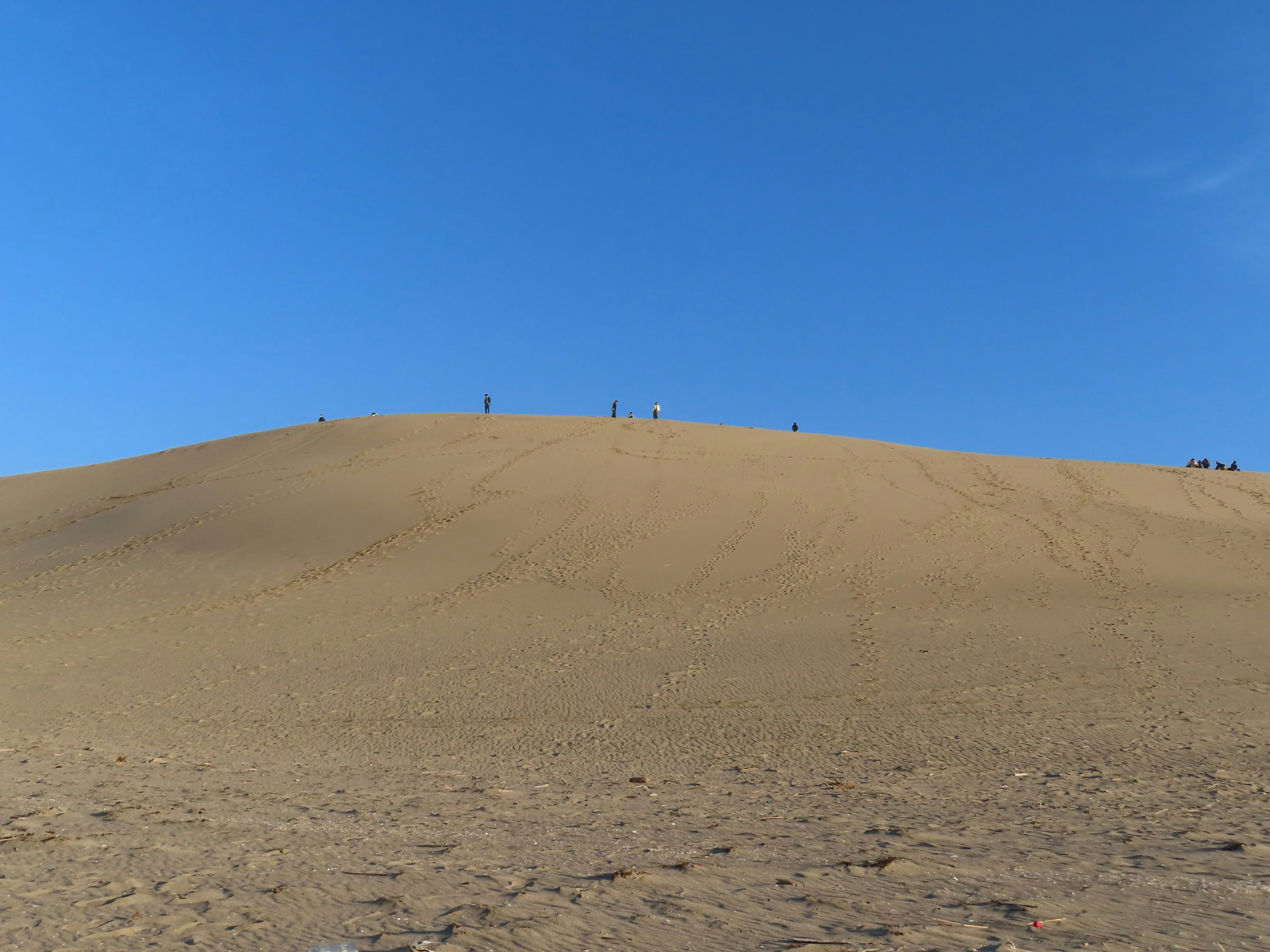 Desert landscape with sand dunes and small figures under blue sky