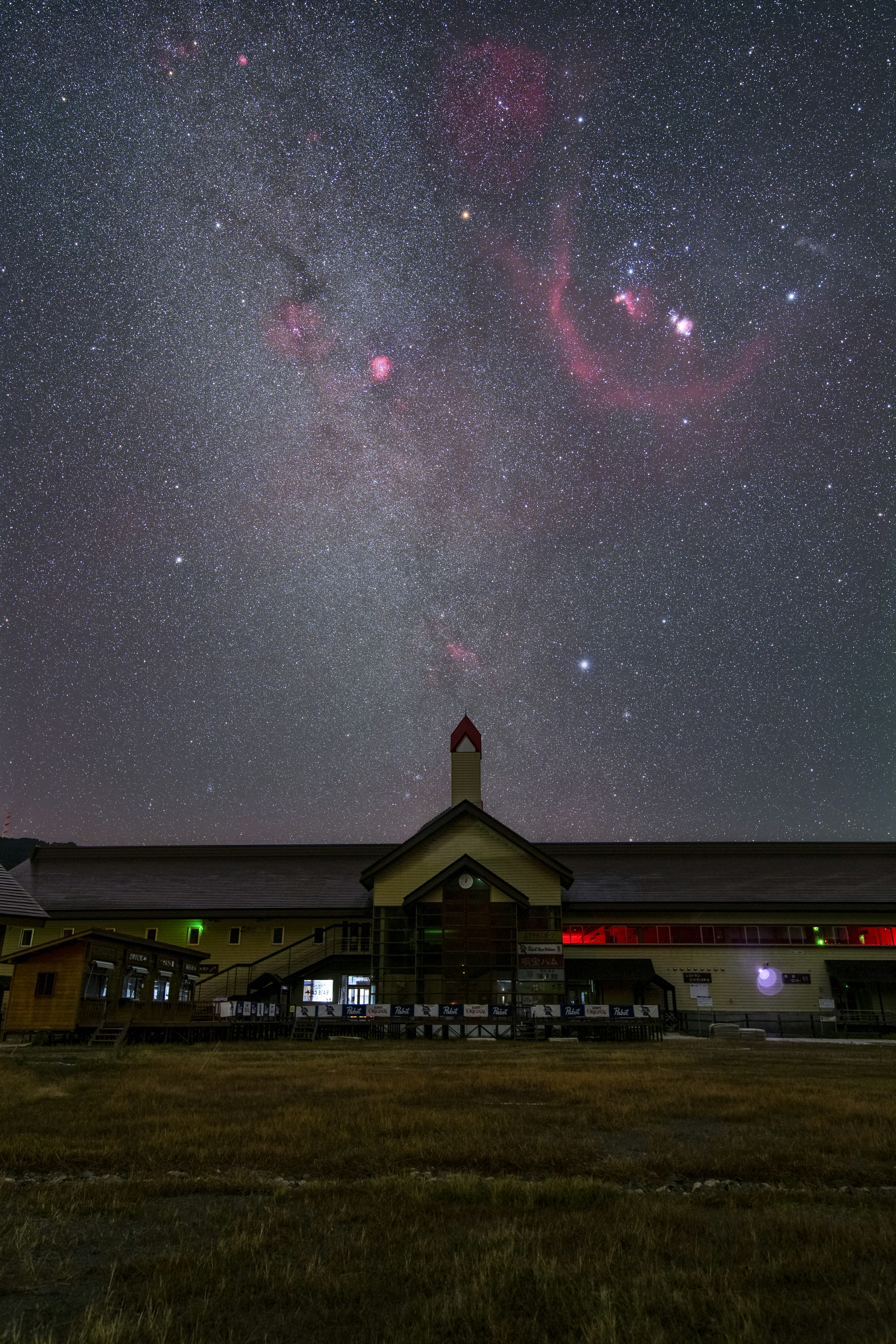 夜空に輝く星々と赤い星雲が見える風景の下に建物がある