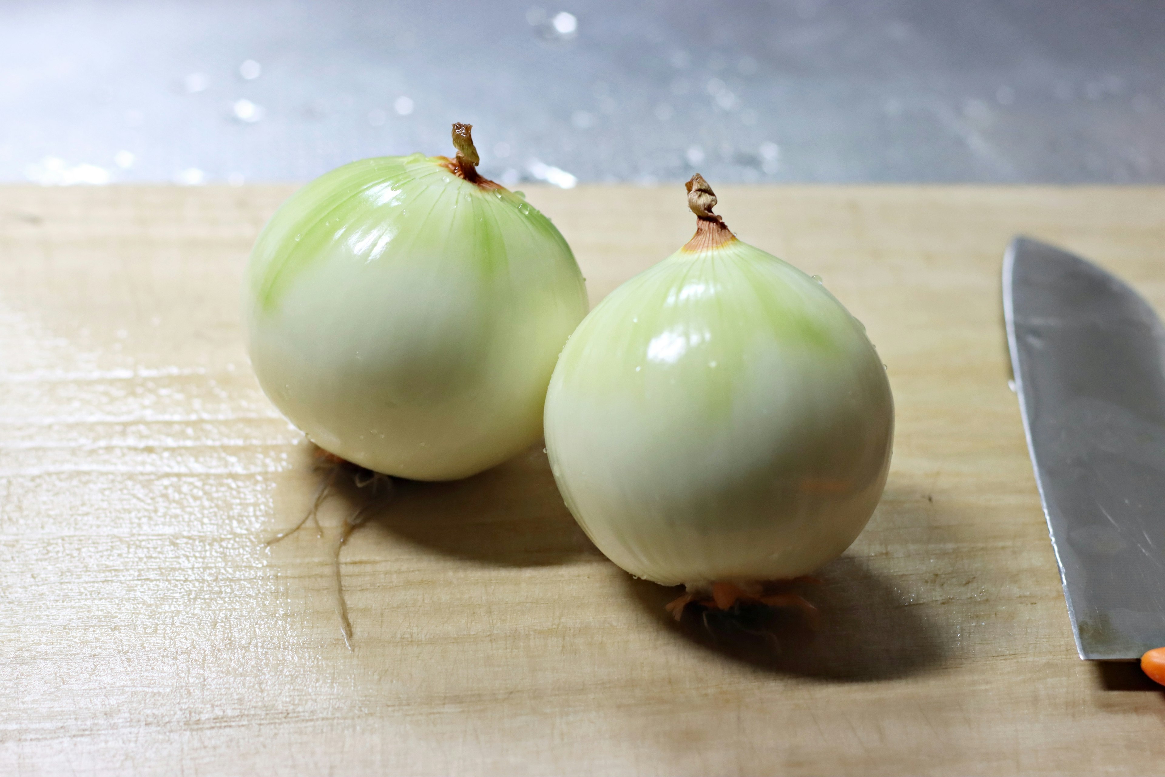 Dua bawang hijau bulat di atas papan pemotong dengan pisau