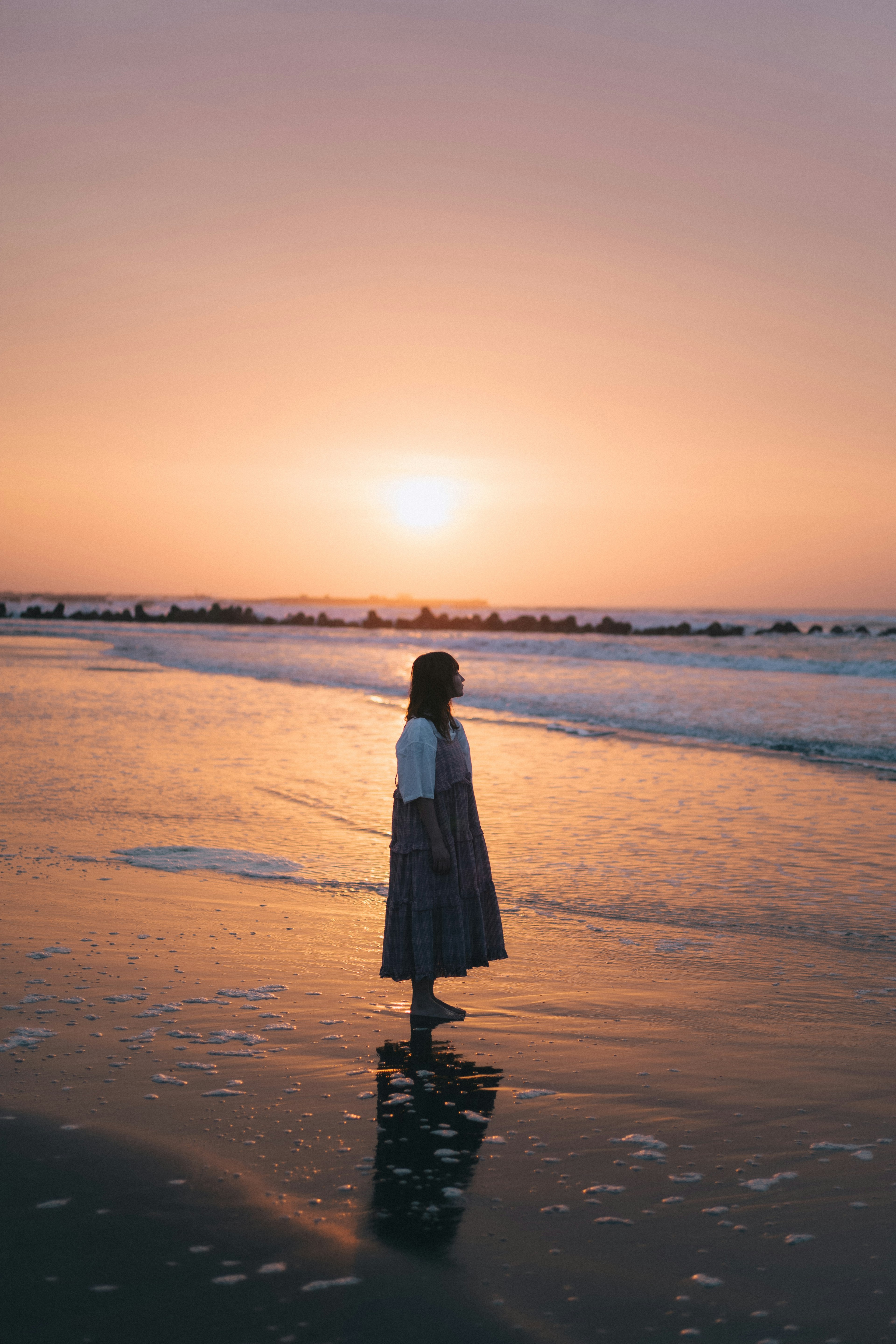 Silhouette d'une femme se tenant sur la plage au coucher du soleil