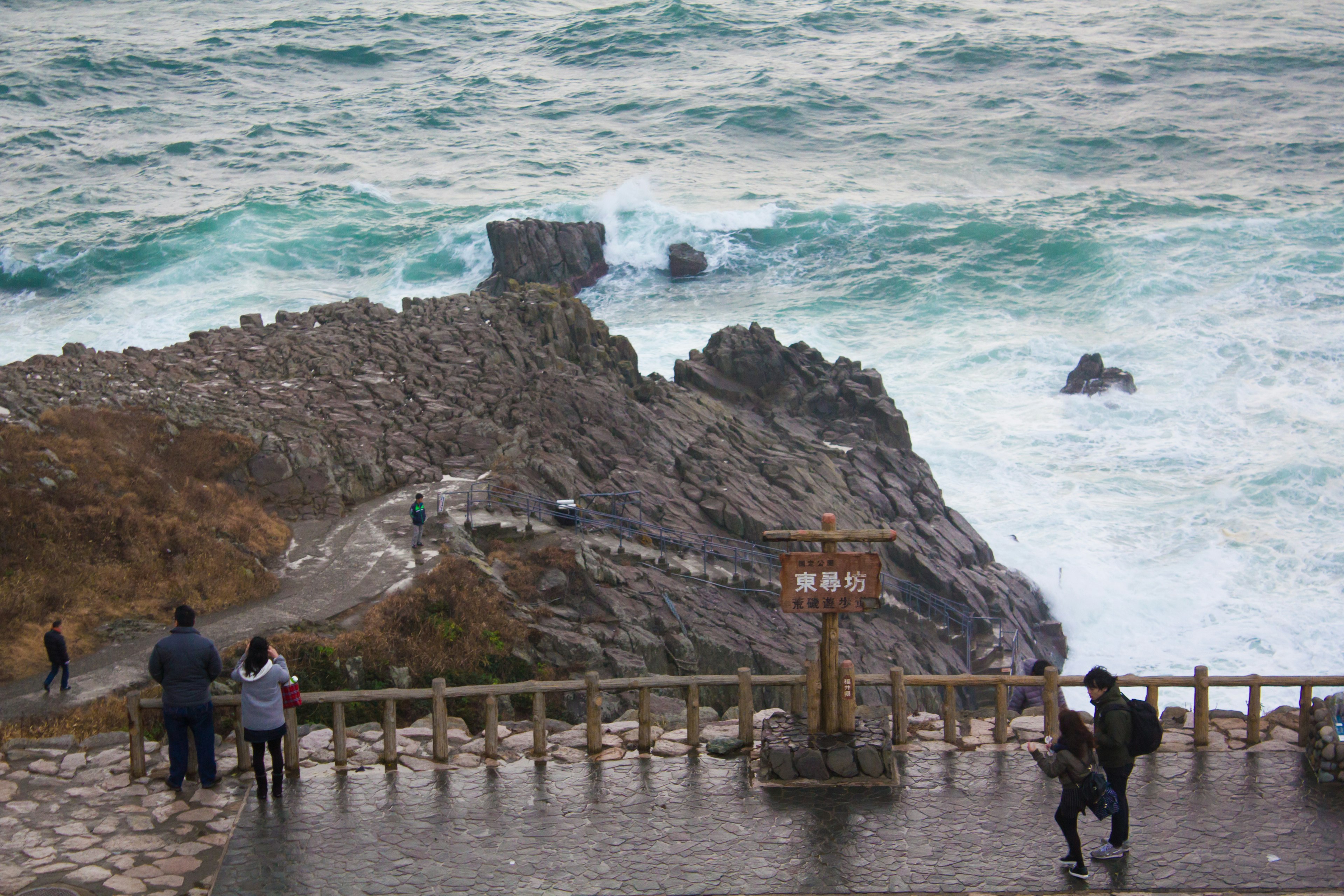 海に面した岩場を見下ろす観光客たちが立っている風景