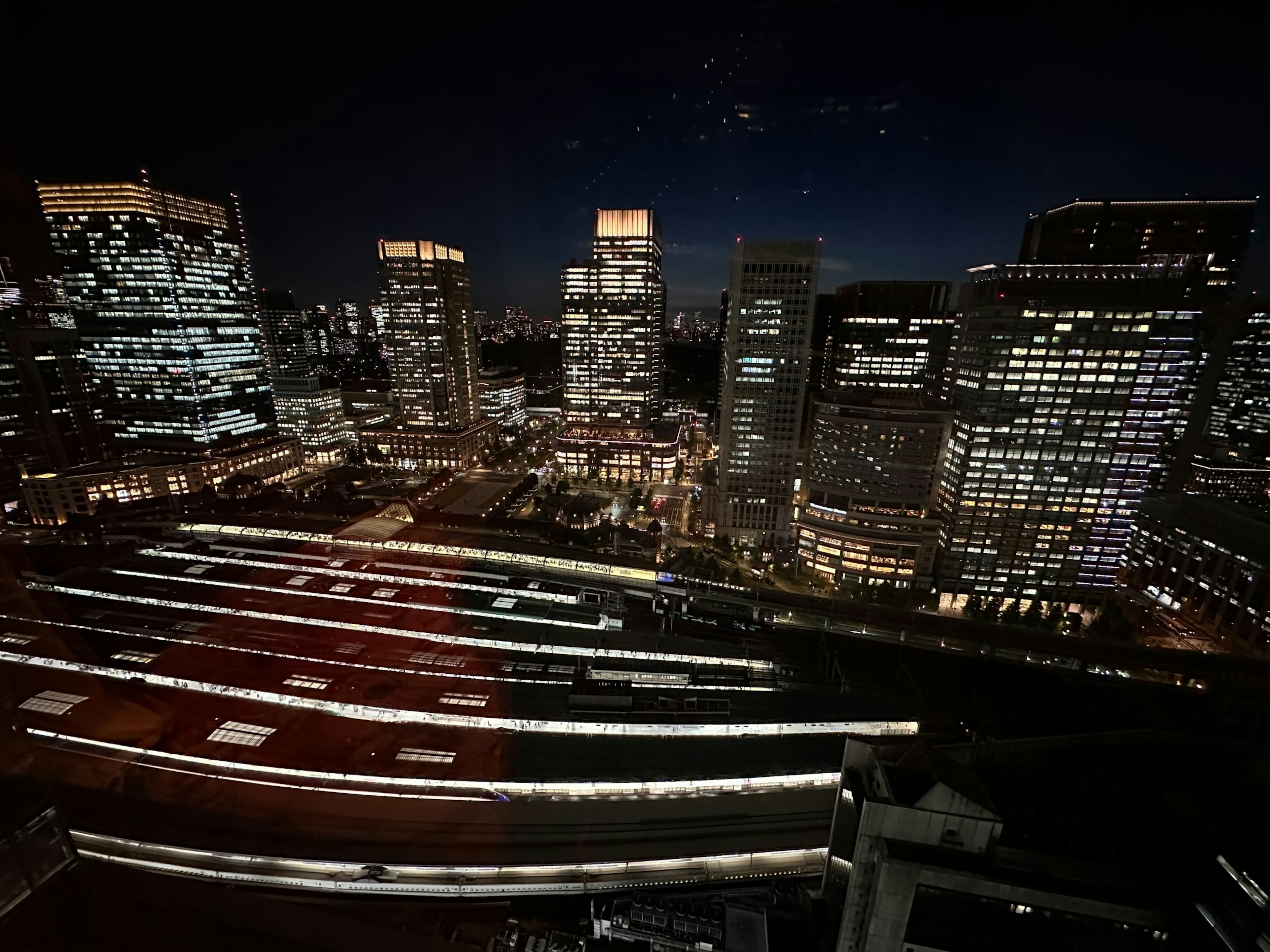 Paisaje urbano nocturno con rascacielos y ventanas iluminadas y una estación de tren iluminada