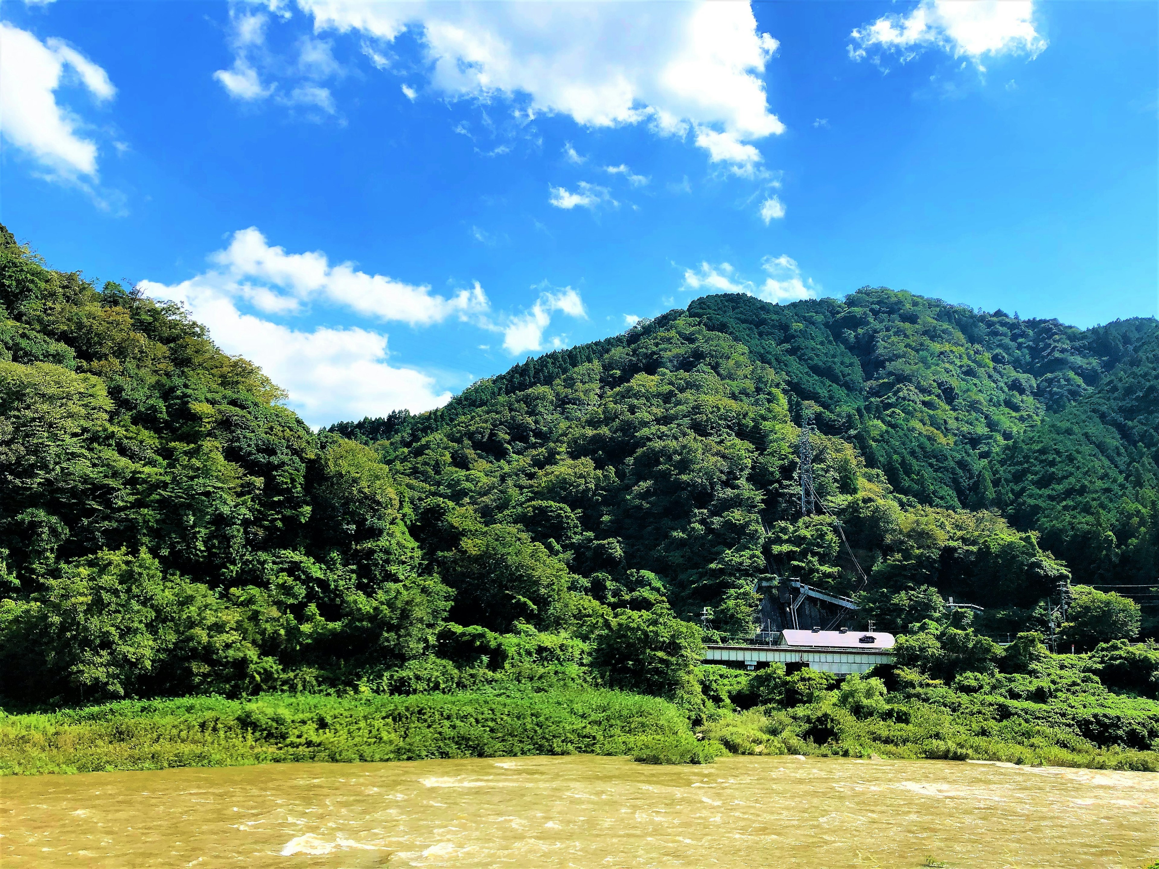 Gunung hijau subur di bawah langit biru dengan sungai