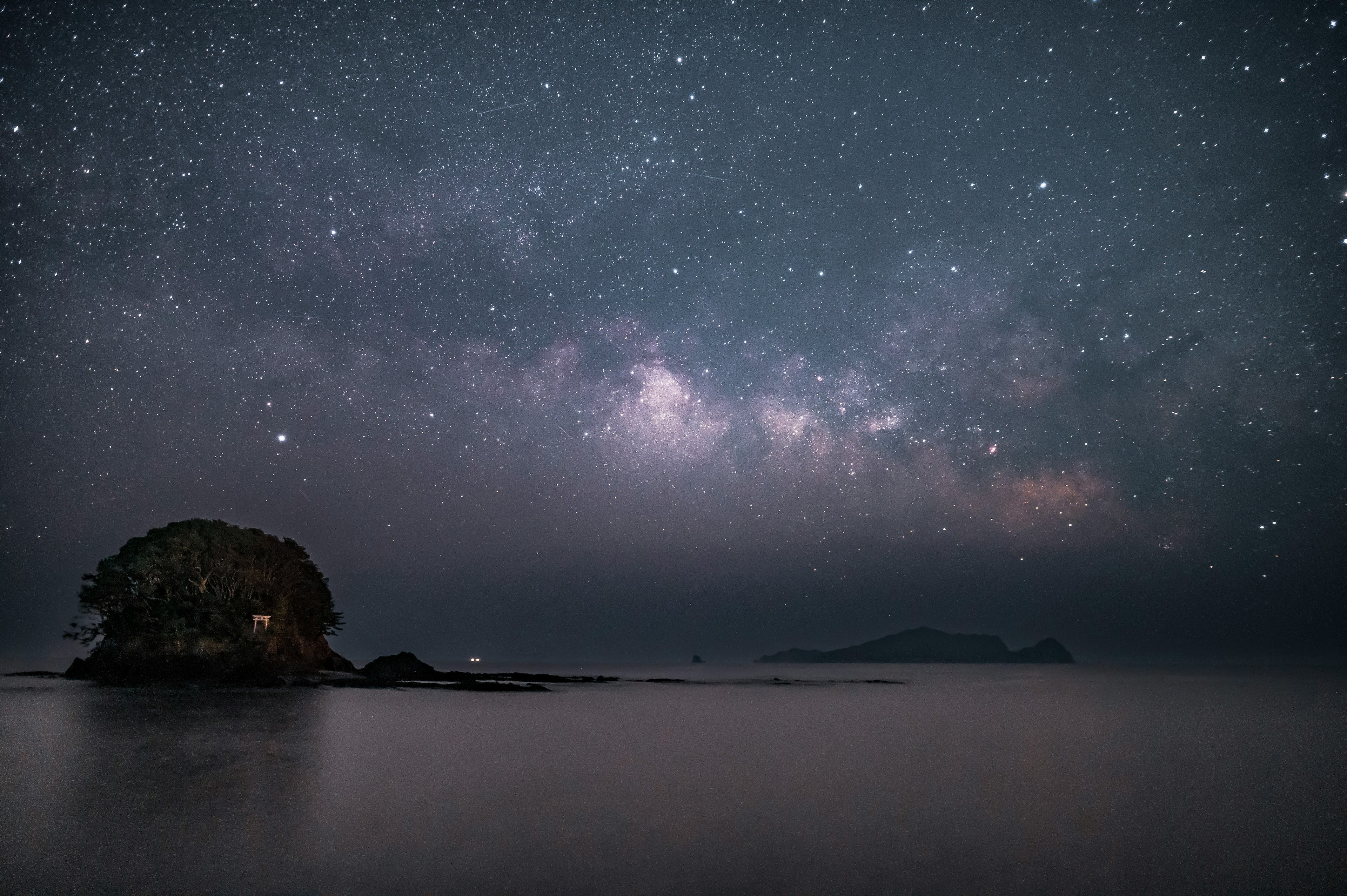 Ein ruhiges Meer unter einem sternenklaren Himmel mit einer kleinen Insel im Vordergrund