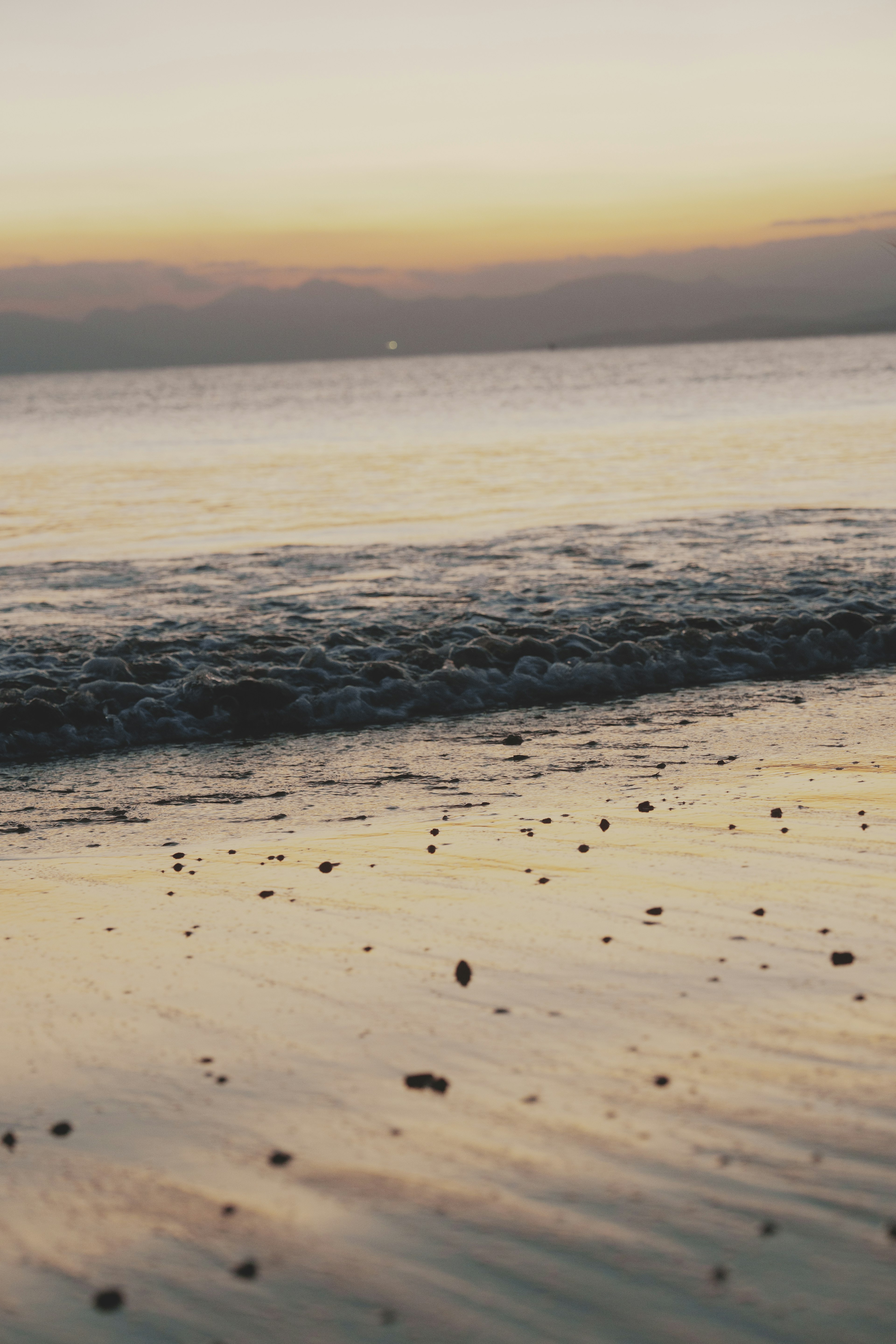 ทิวทัศน์ชายหาดที่สงบในยามพระอาทิตย์ตกคลื่นอ่อนๆซัดเข้าชายหาดที่เต็มไปด้วยก้อนกรวด