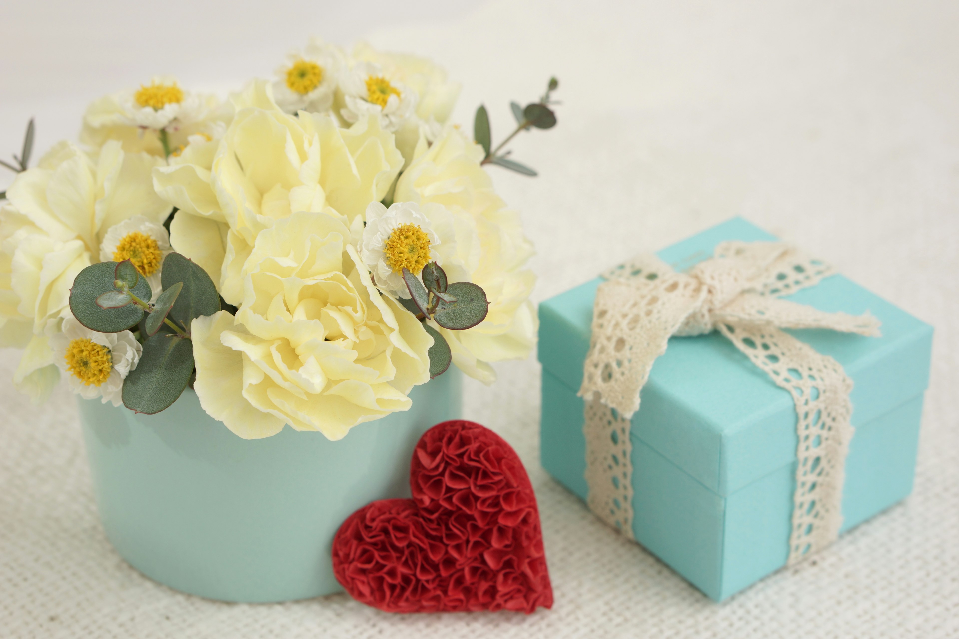 Blue vase with yellow flowers and small green leaves arrangement Red heart-shaped decoration and blue gift box with ribbon