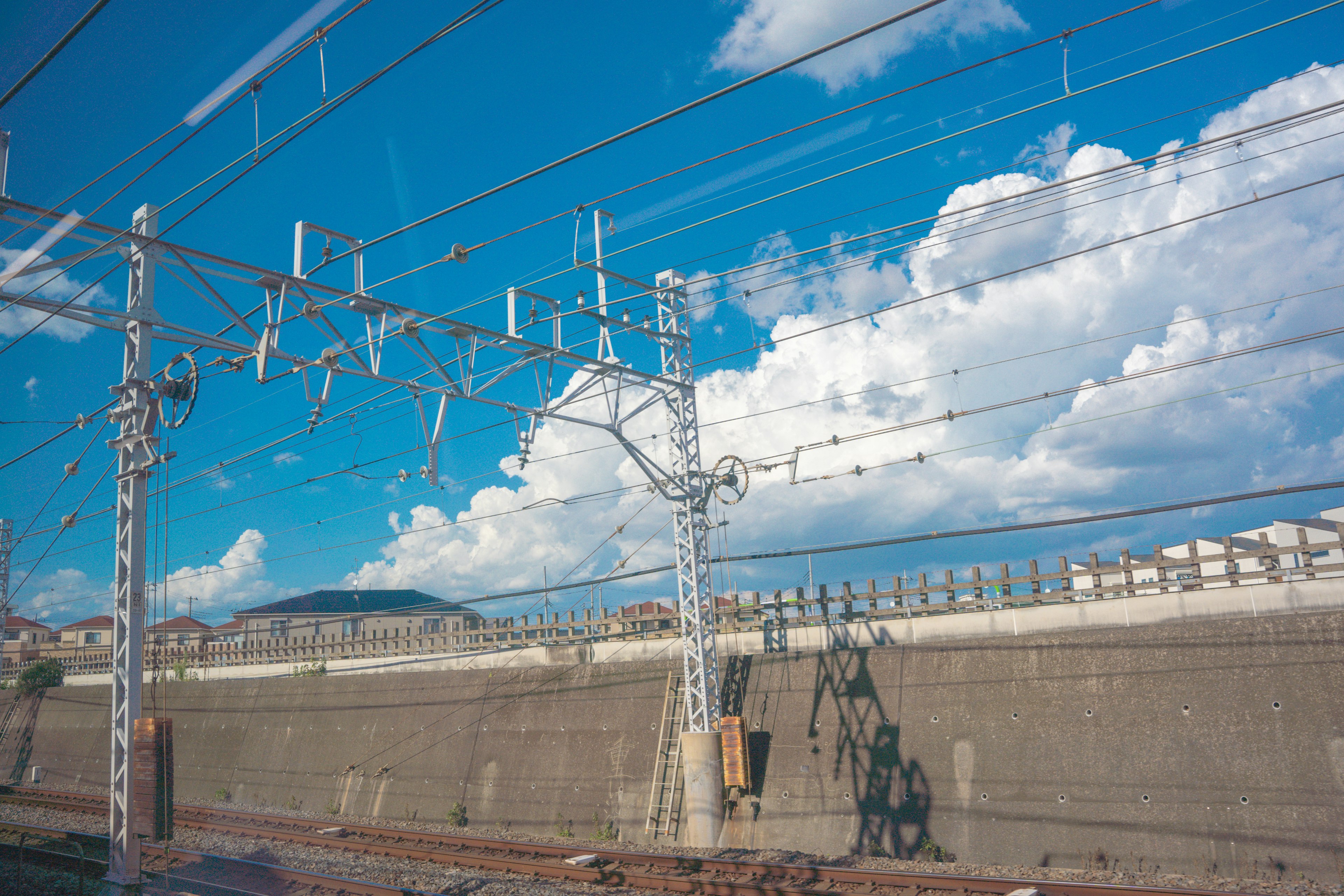 青空と白い雲を背景にした鉄道の架線とコンクリートの壁