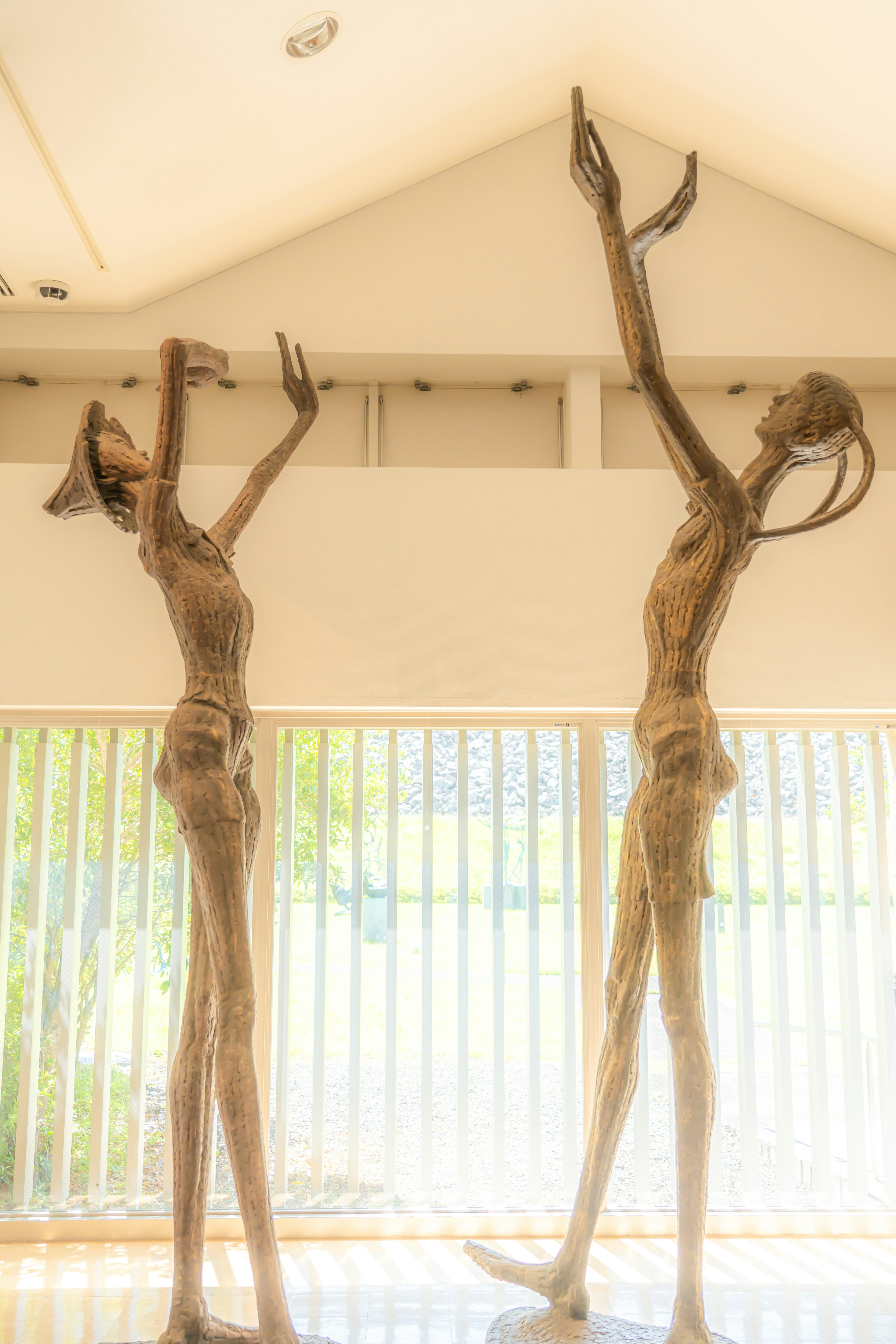 Deux grandes sculptures en bois tendant les bras vers le plafond