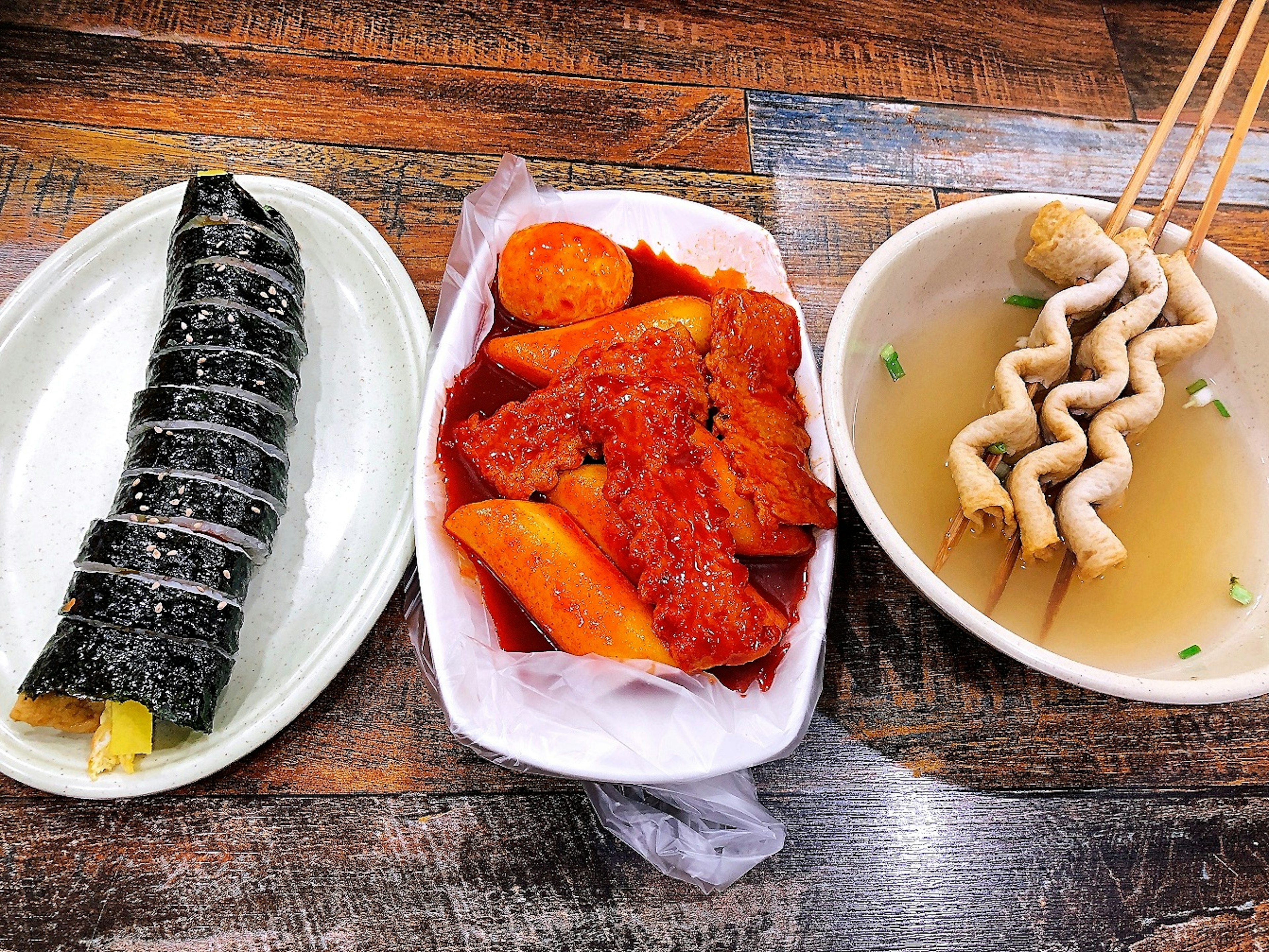 Three Korean dishes including gimbap, spicy radish, and fish cake soup