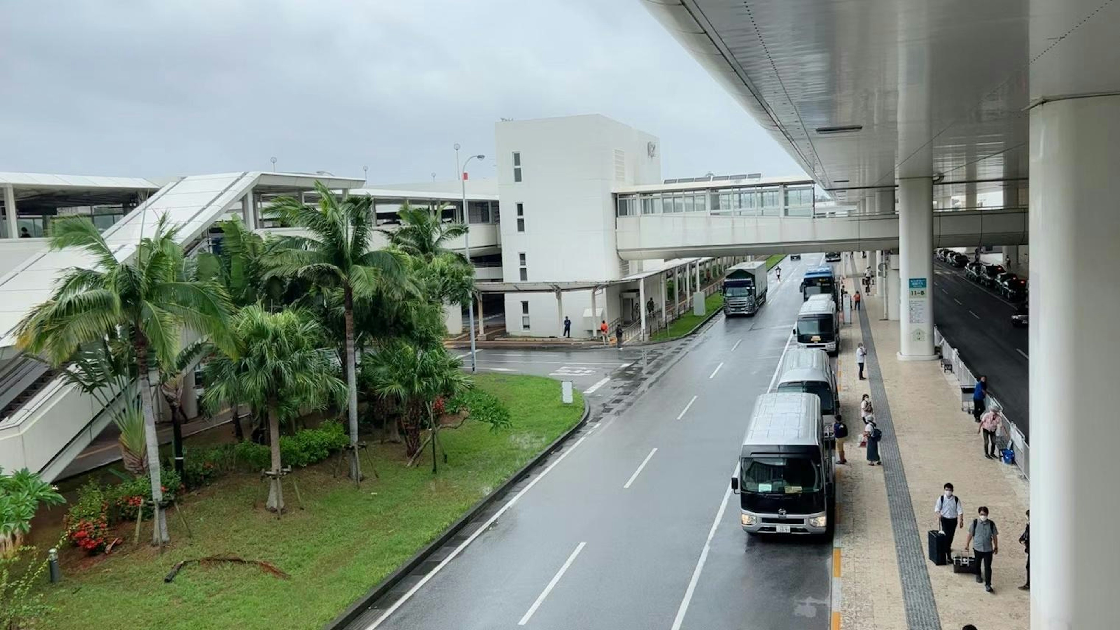 View of an airport building and bus stop with rain falling green plants nearby