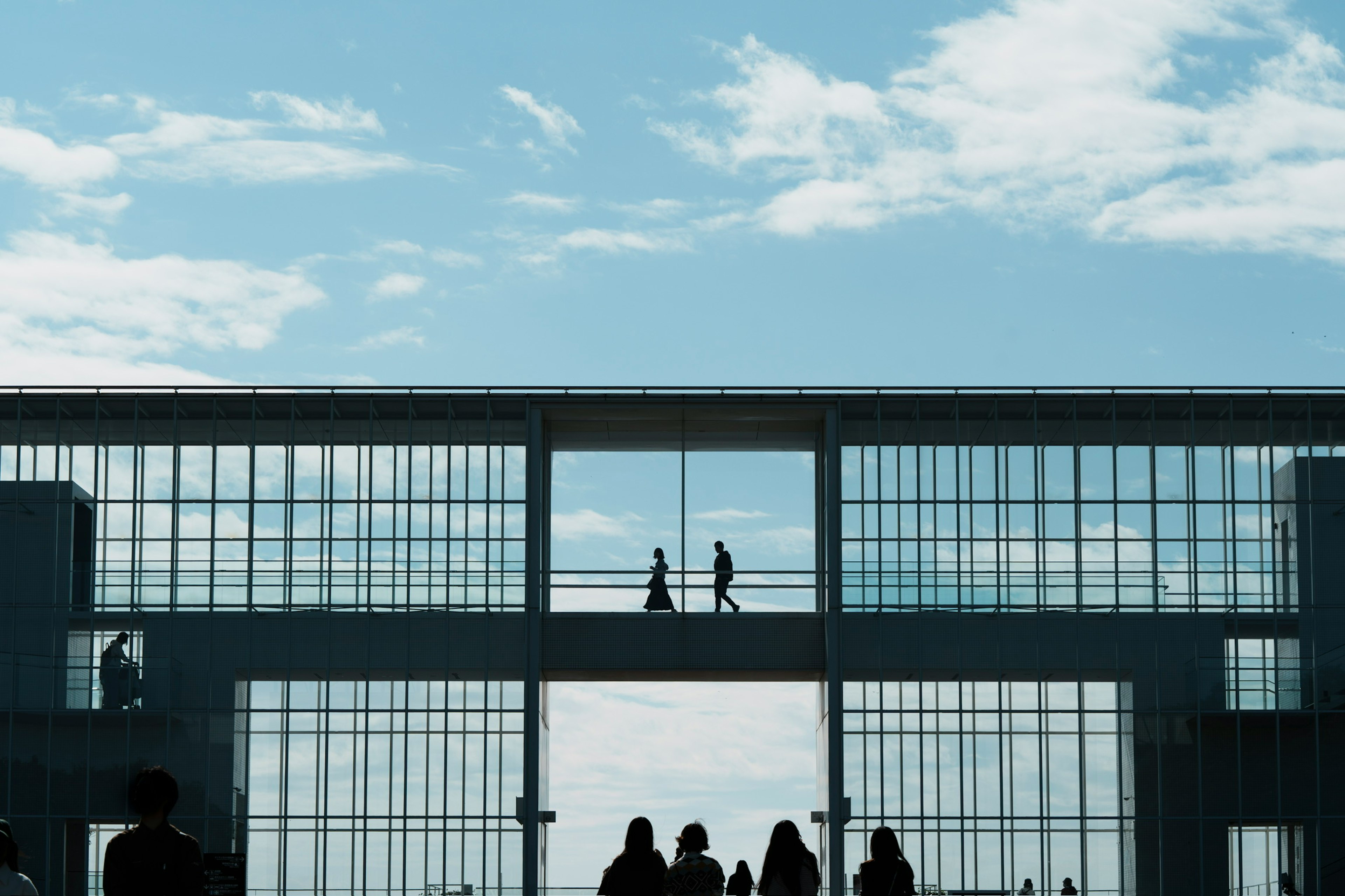 Silhouettes de personnes marchant contre un bâtiment en verre sous un ciel bleu