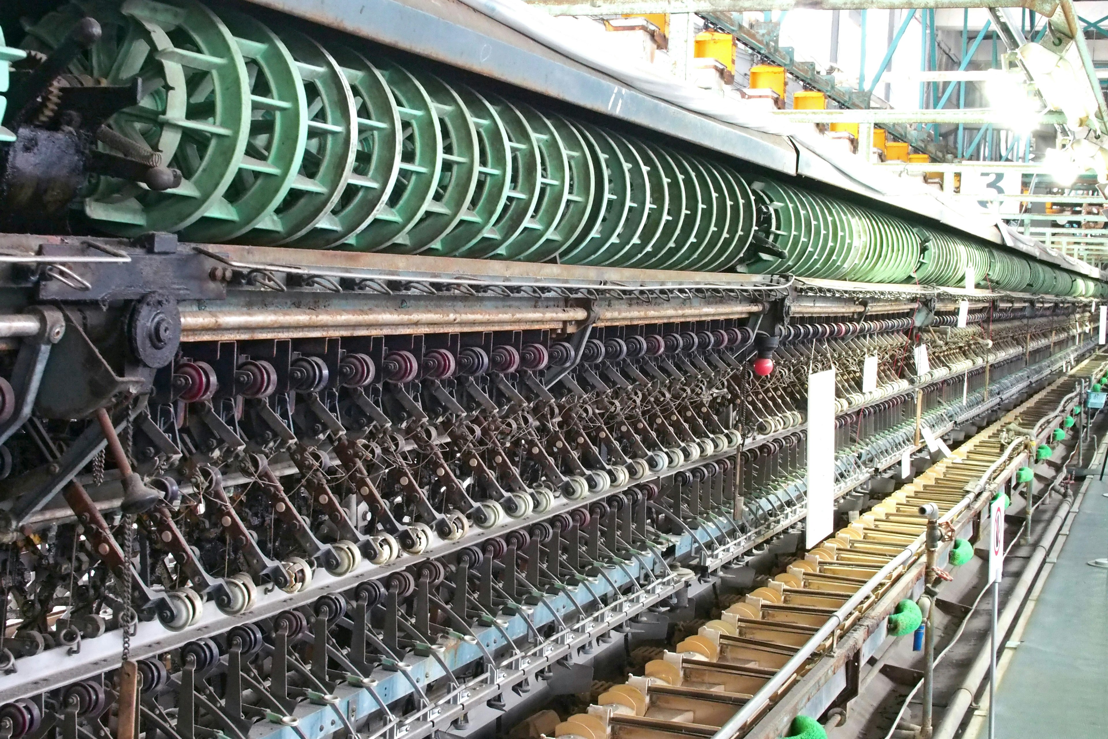 Interior view of a complex spinning machine with green rollers and metal components