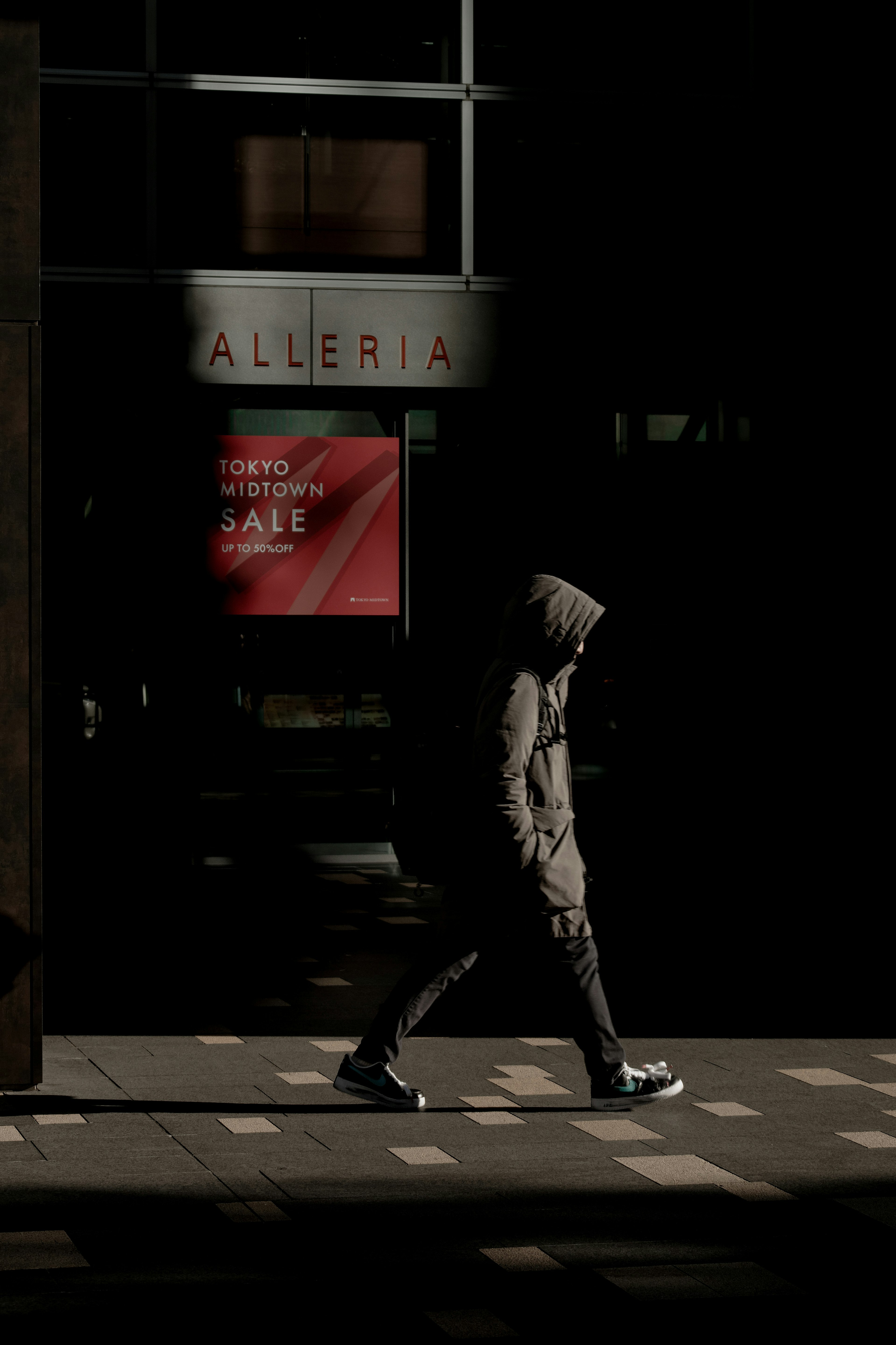 Una figura con capucha caminando en una calle poco iluminada con sombras contrastantes