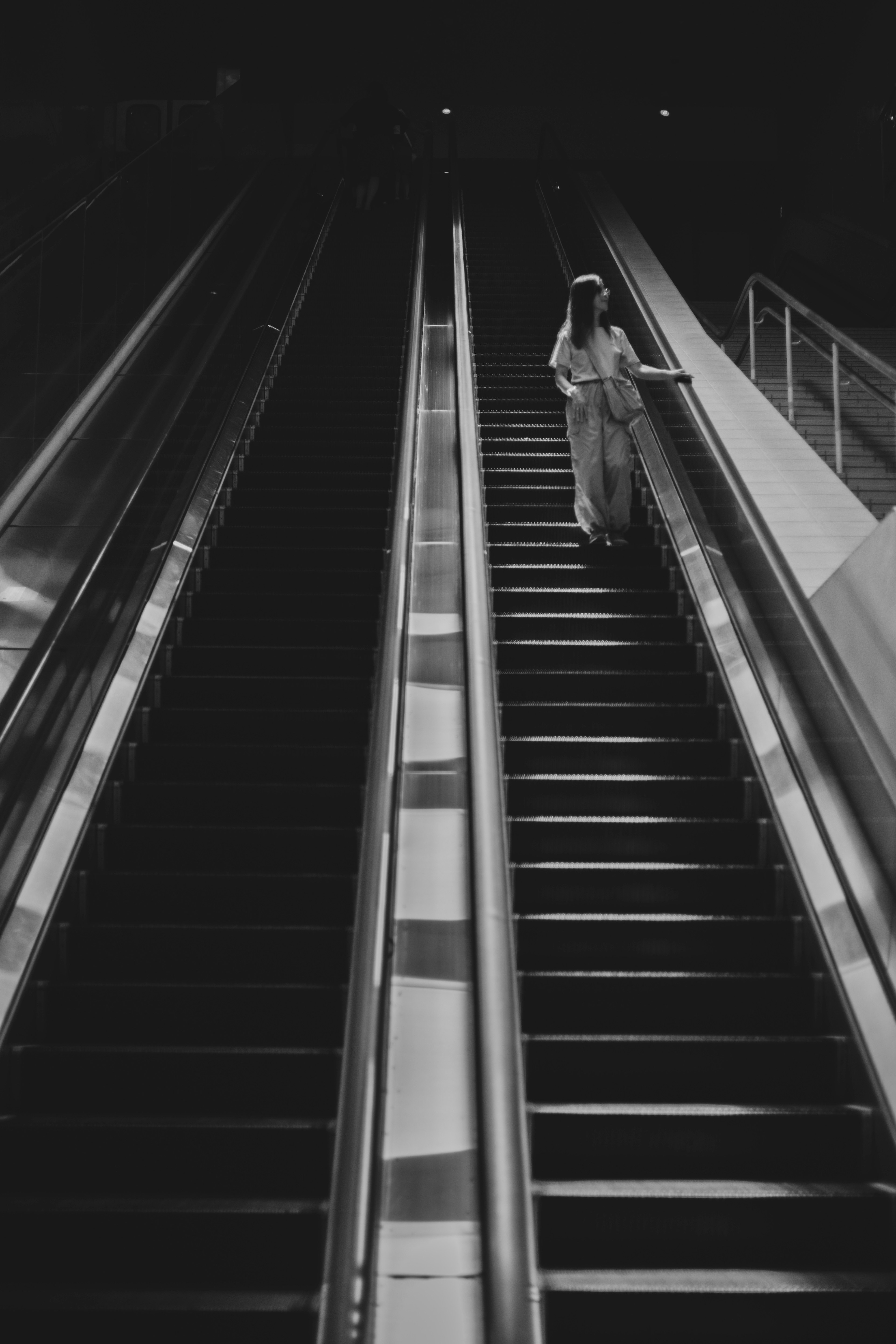 Foto en blanco y negro de una persona subiendo una escalera mecánica en un entorno oscuro