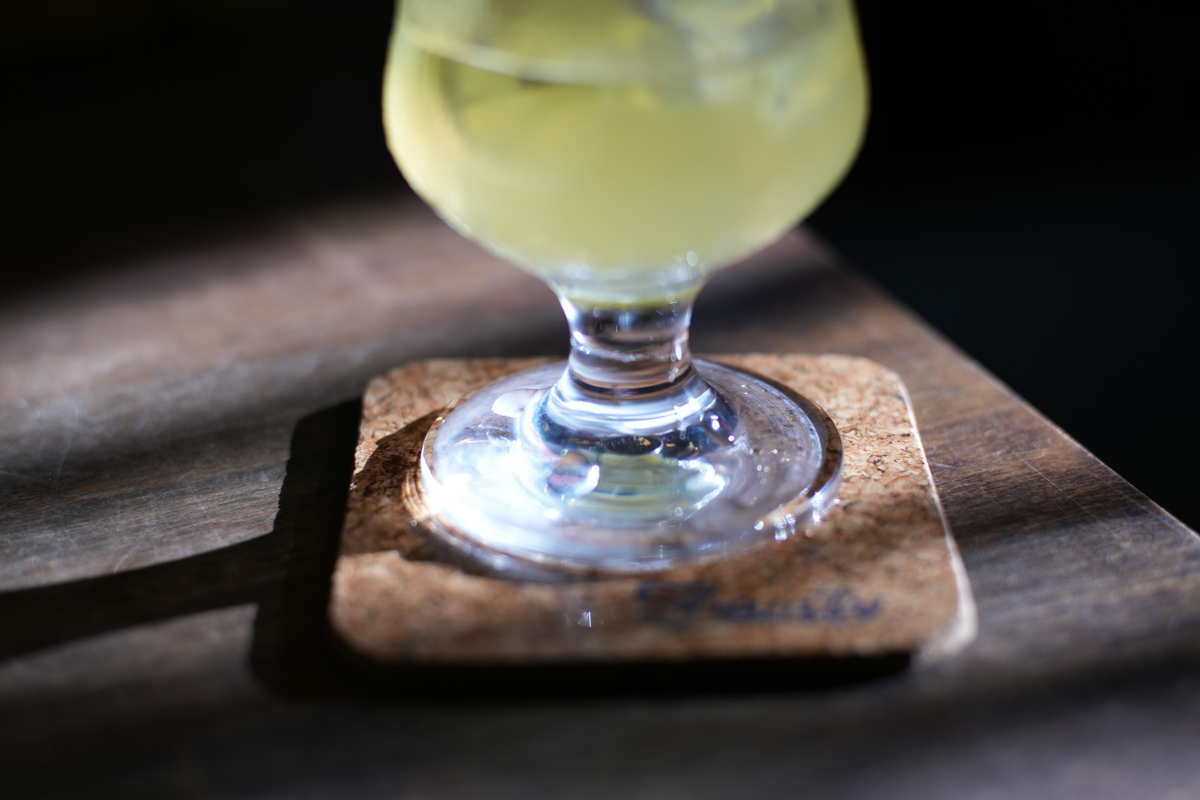 Image of a glass with ice and a drink on a wooden coaster