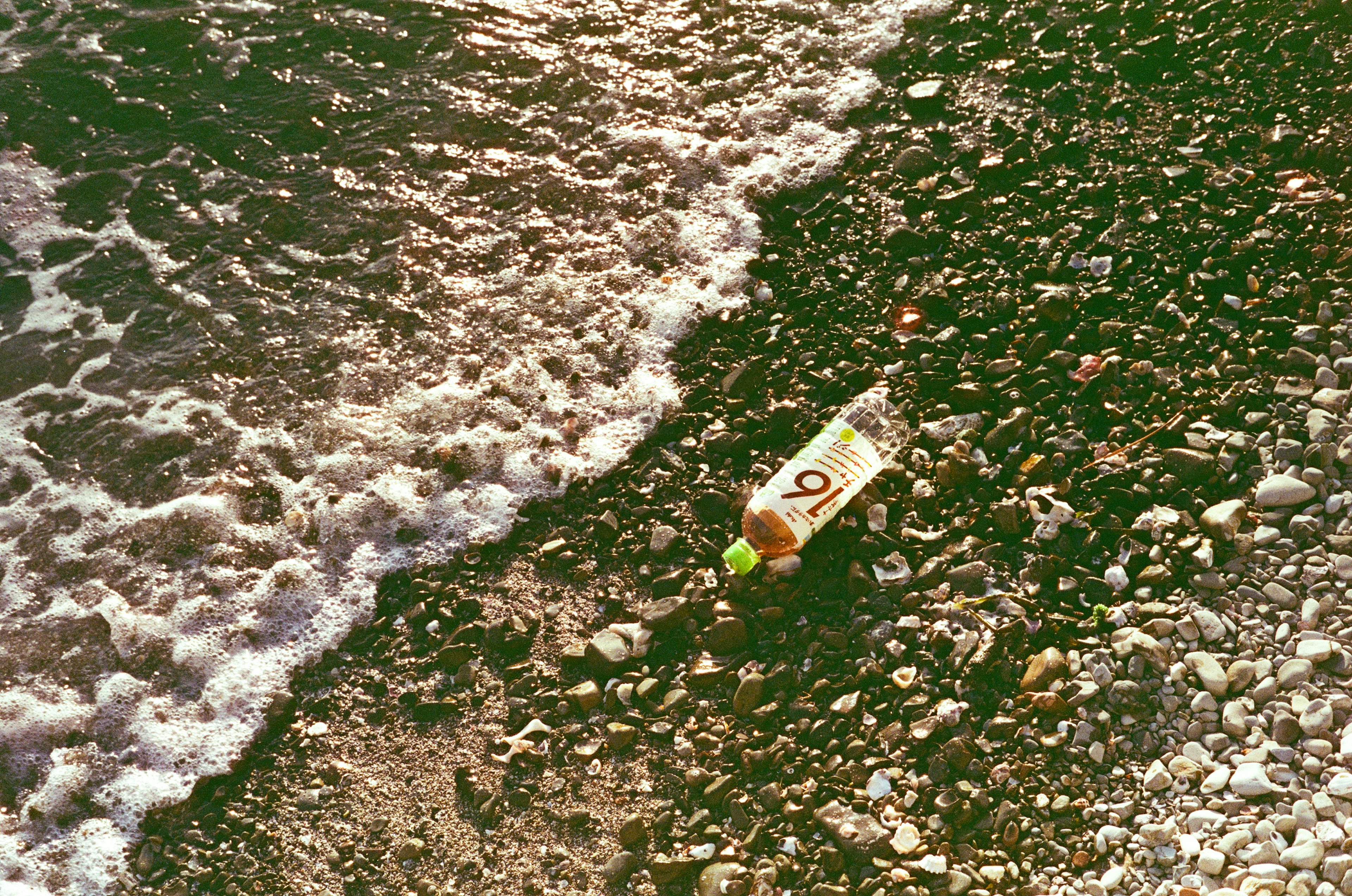 Bouteille en plastique échouée parmi les galets et les vagues