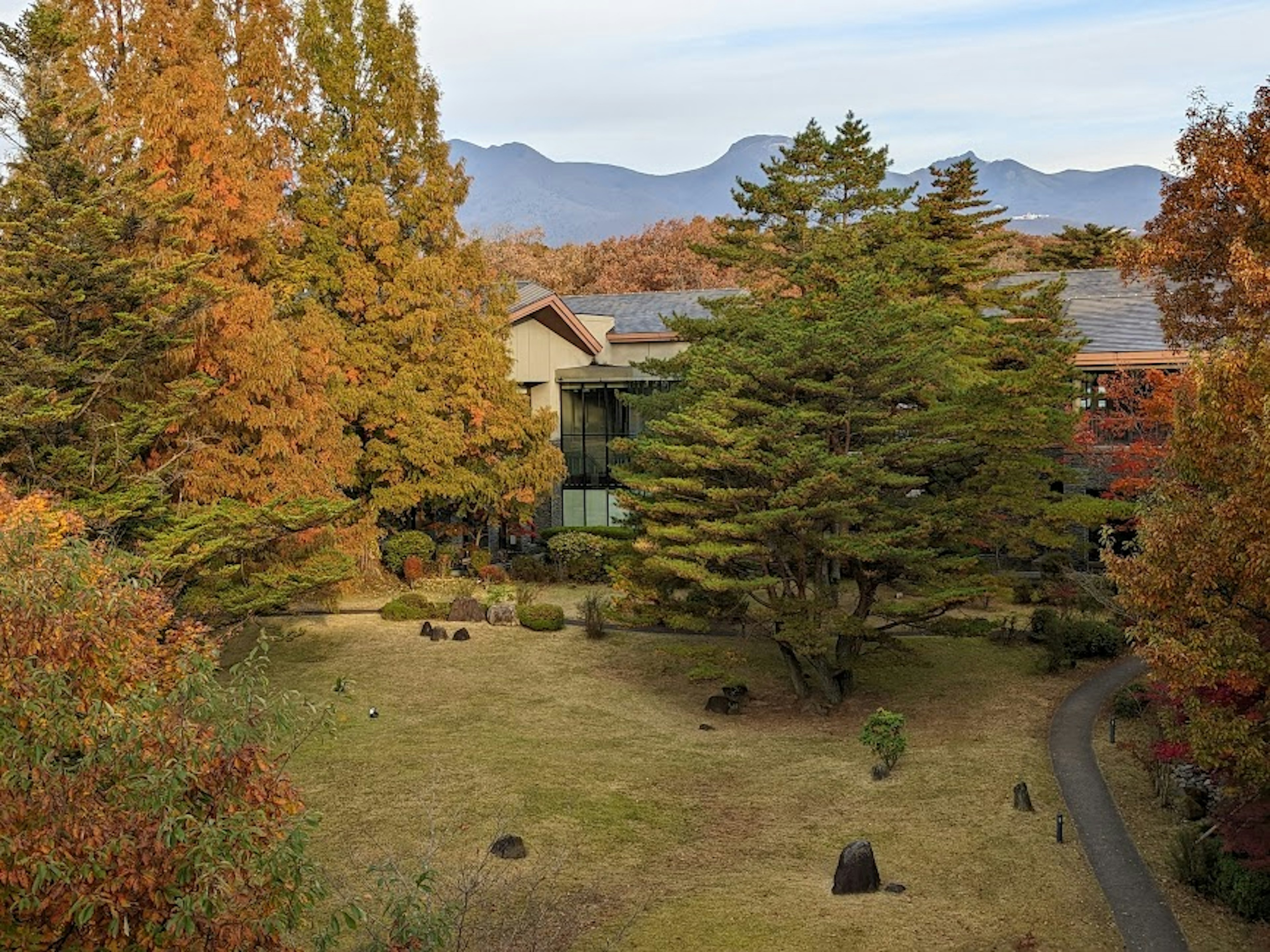 秋の色合いの木々と山々を背景にした庭のある建物