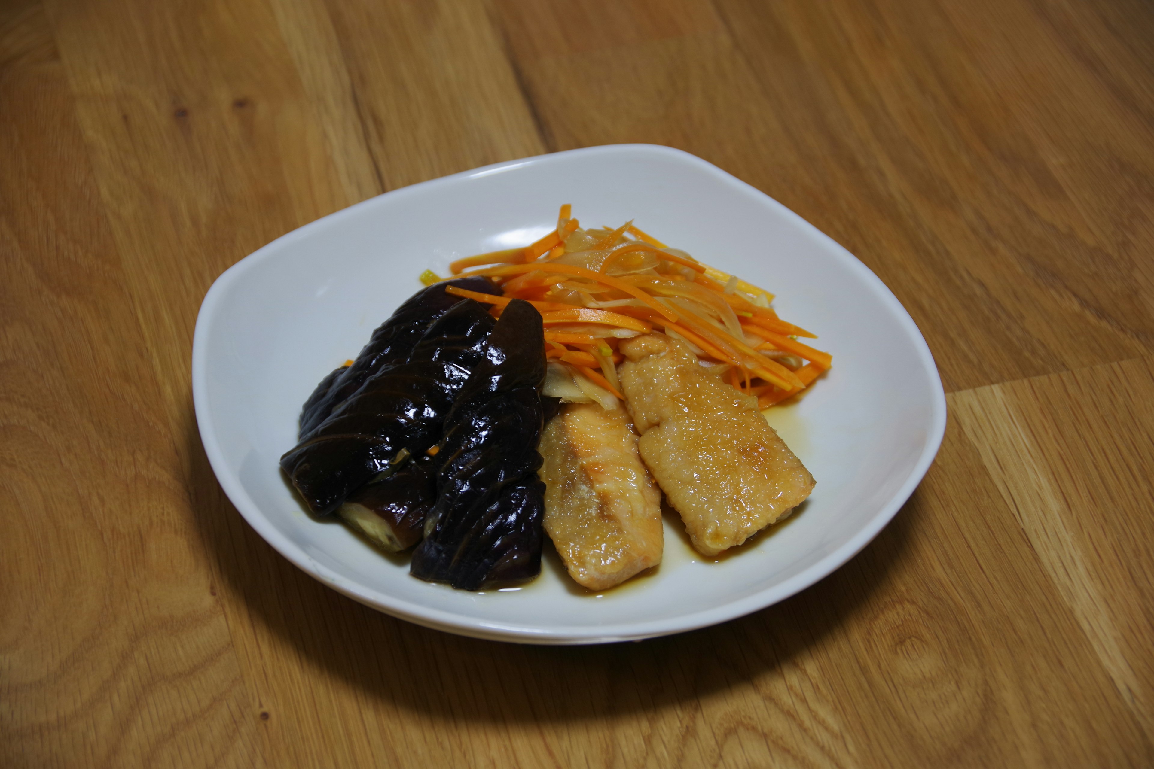 Pescado frito con salsa negra y zanahorias ralladas en un plato blanco