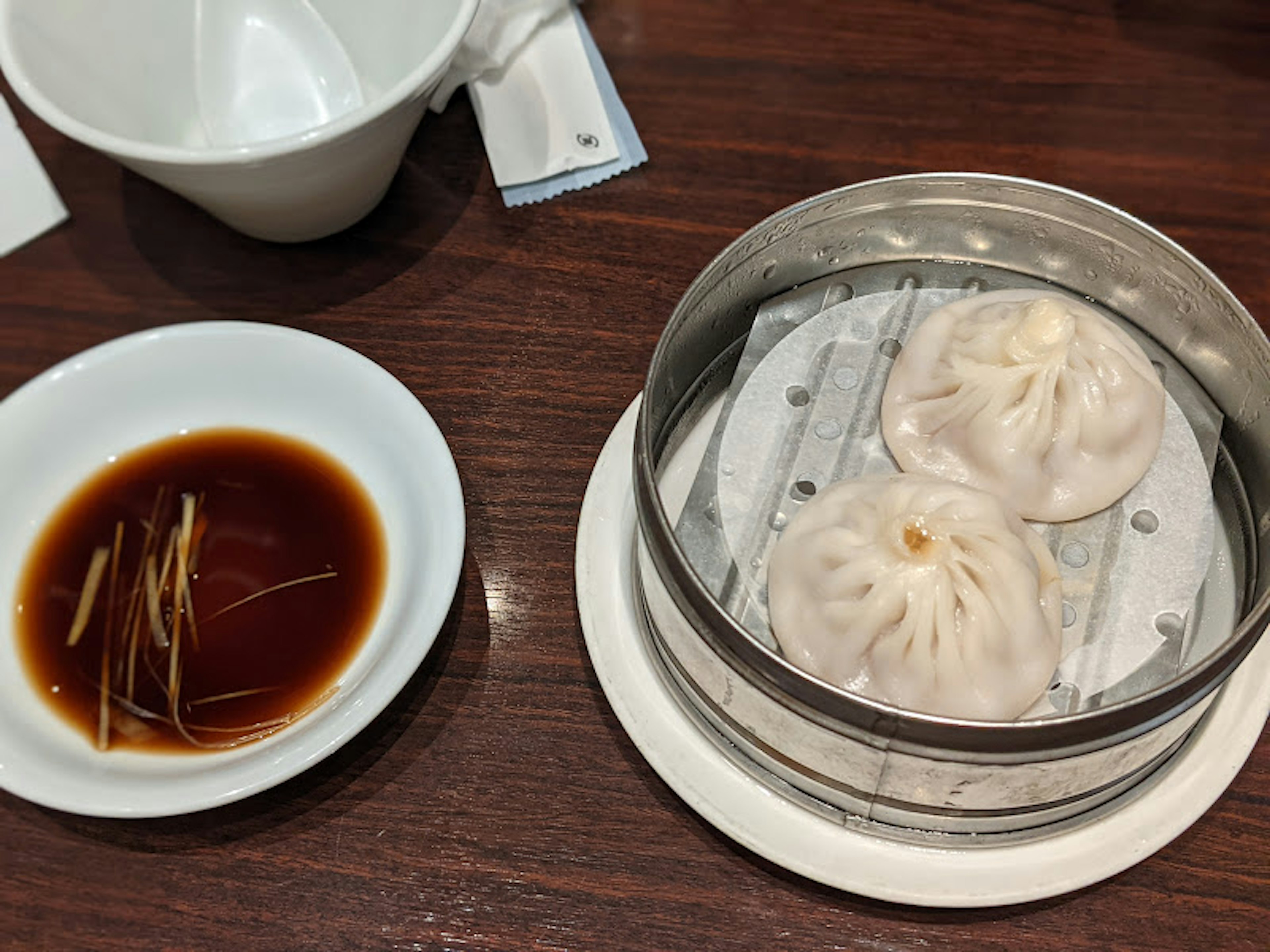 Steamed dumplings in a bamboo steamer with soy sauce and ginger on the side