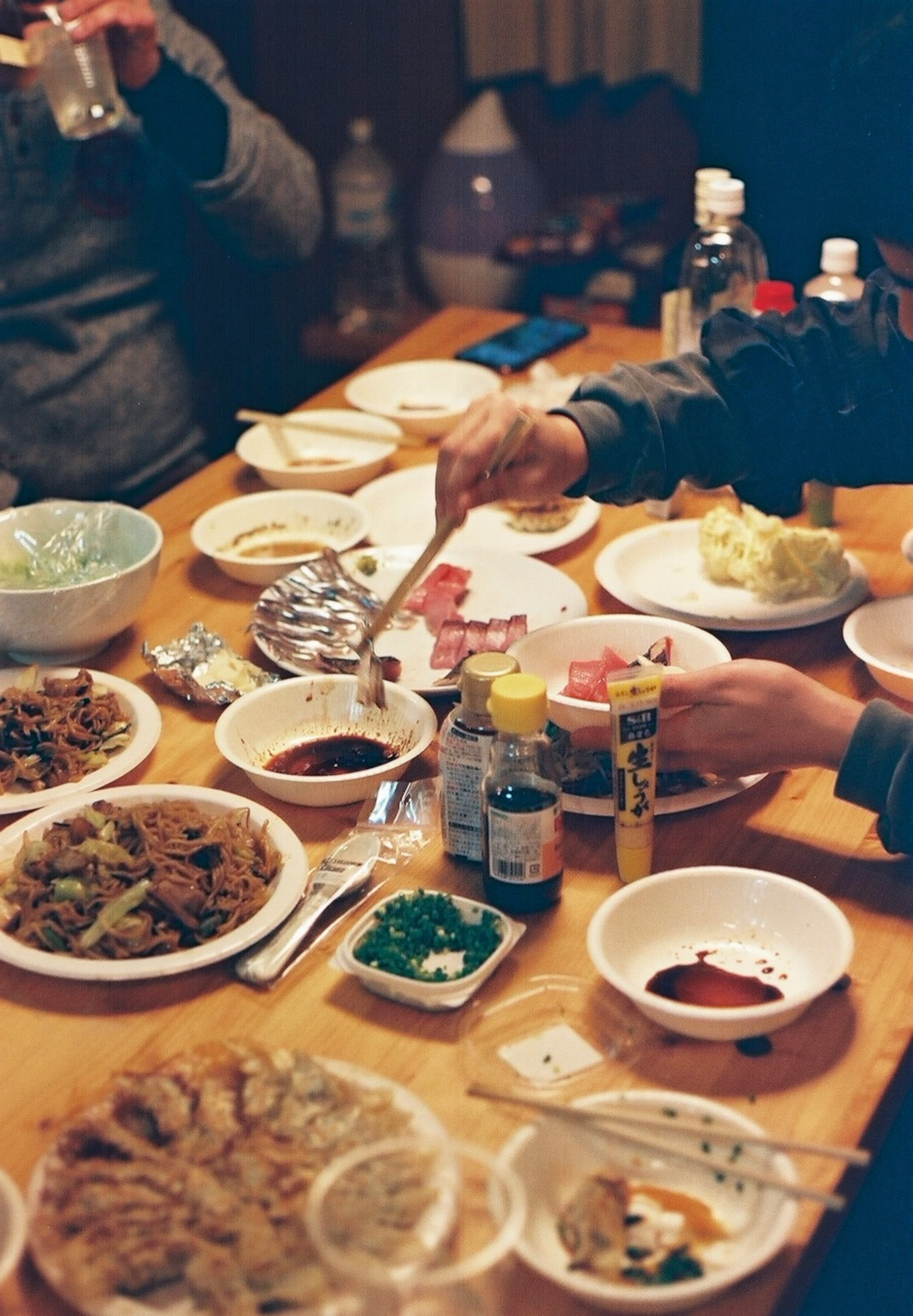 Hands reaching for various dishes and sauces on a wooden table