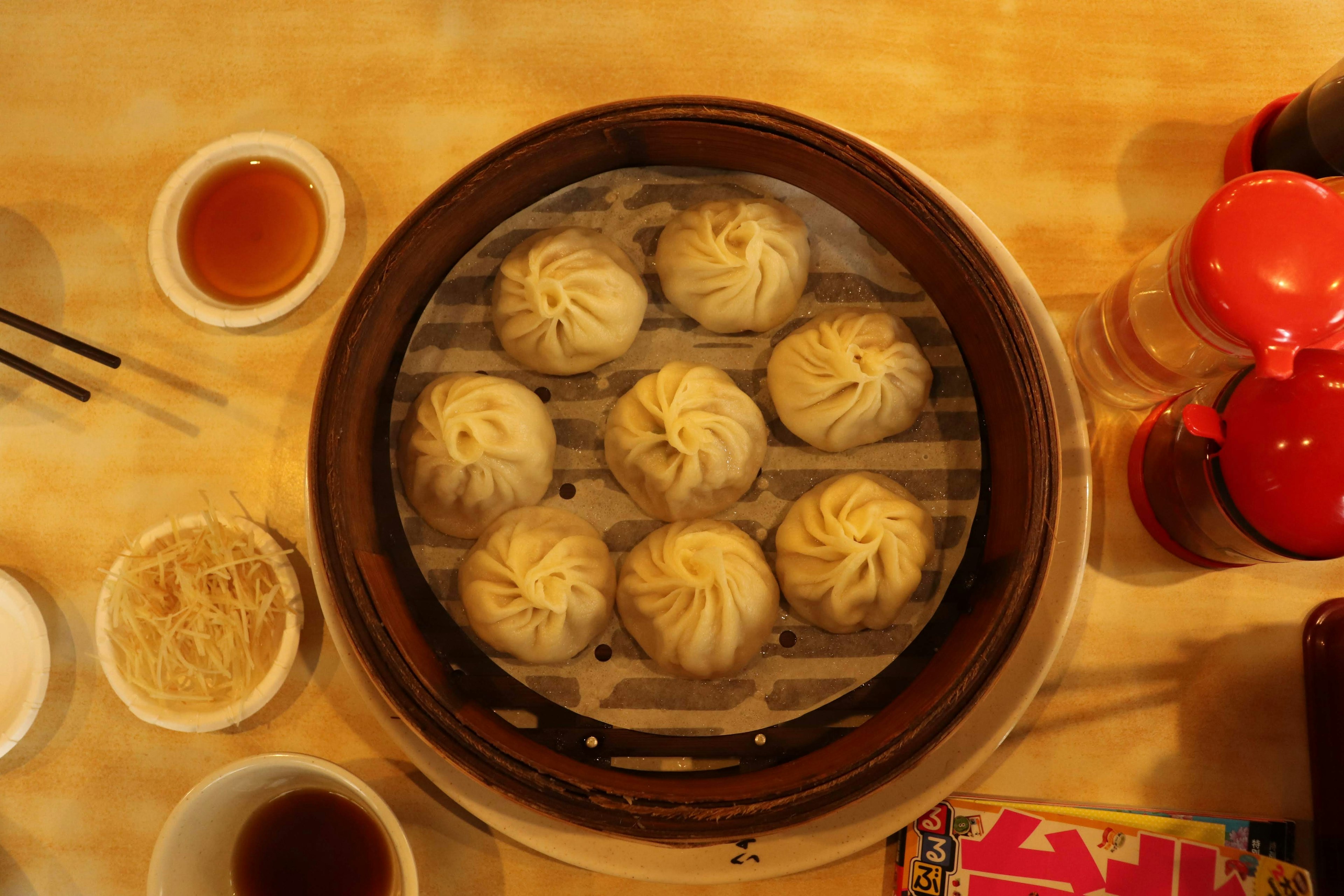 Steamed buns arranged in a bamboo steamer with condiments on the side