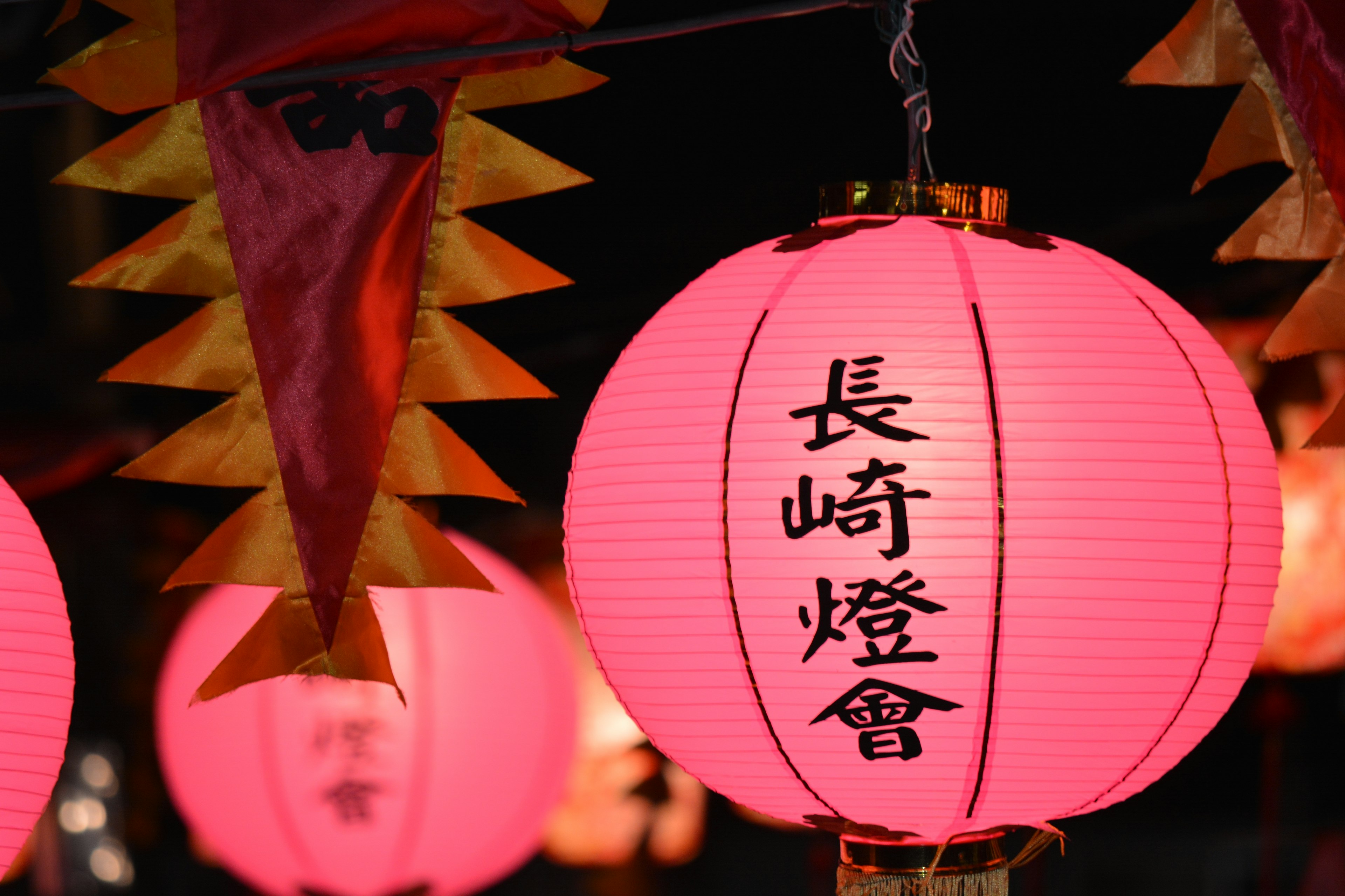 Pink lantern glowing at night with 長崎燈會 text