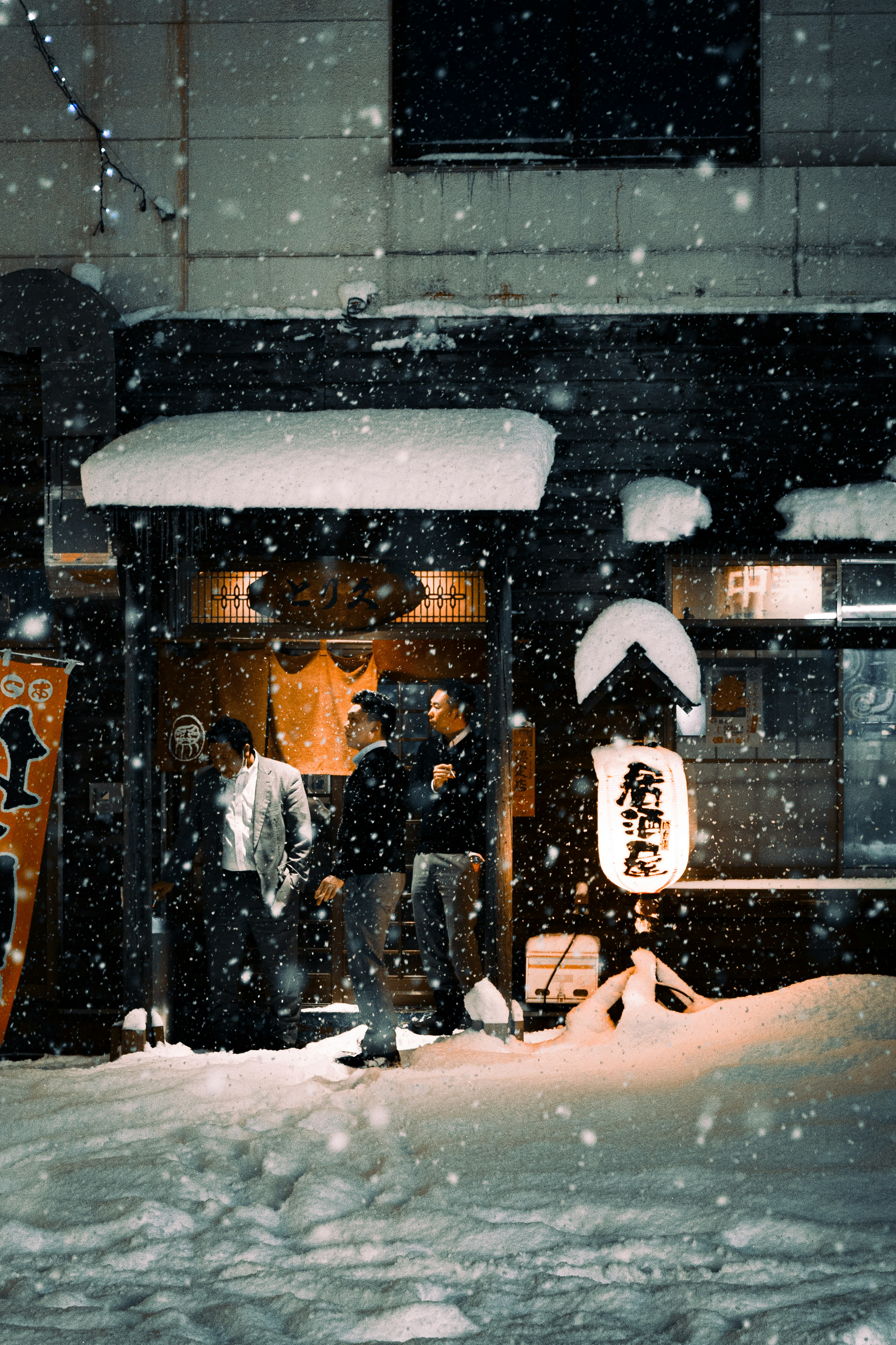 Personas de pie frente a un restaurante japonés en una noche nevada