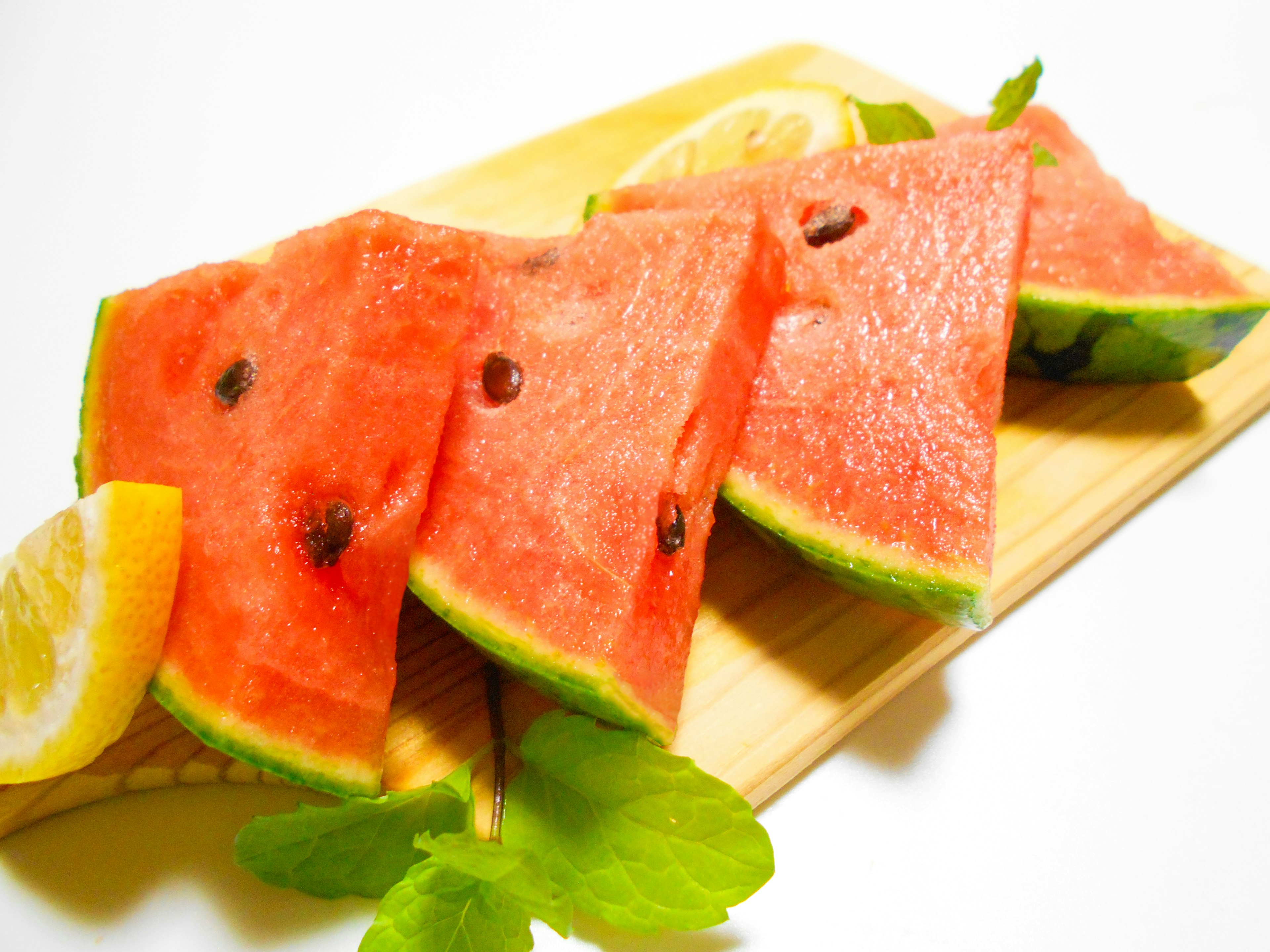 Fresh watermelon slices and lemon wedges arranged on a wooden cutting board