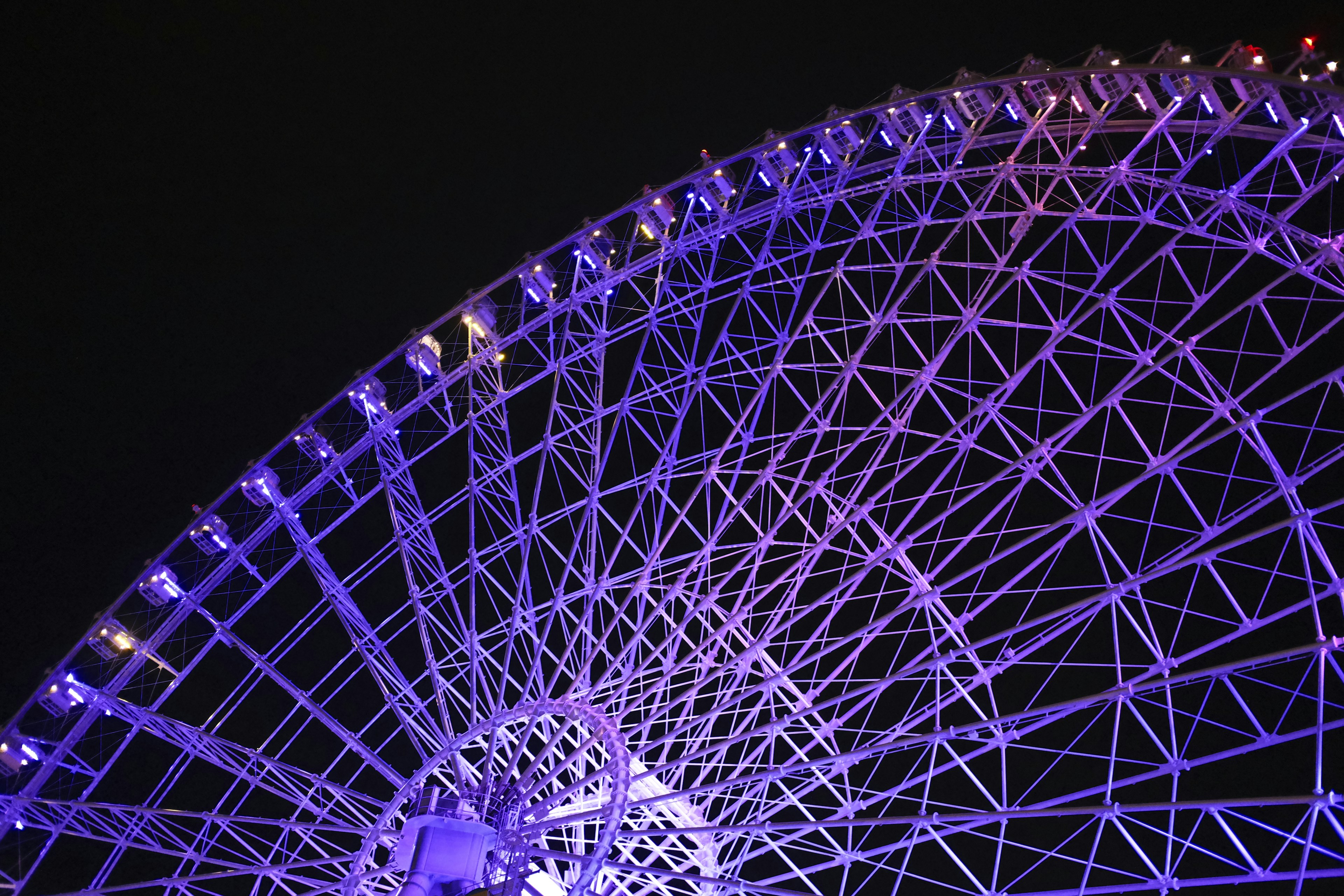 Purple illuminated ferris wheel structure against the night sky