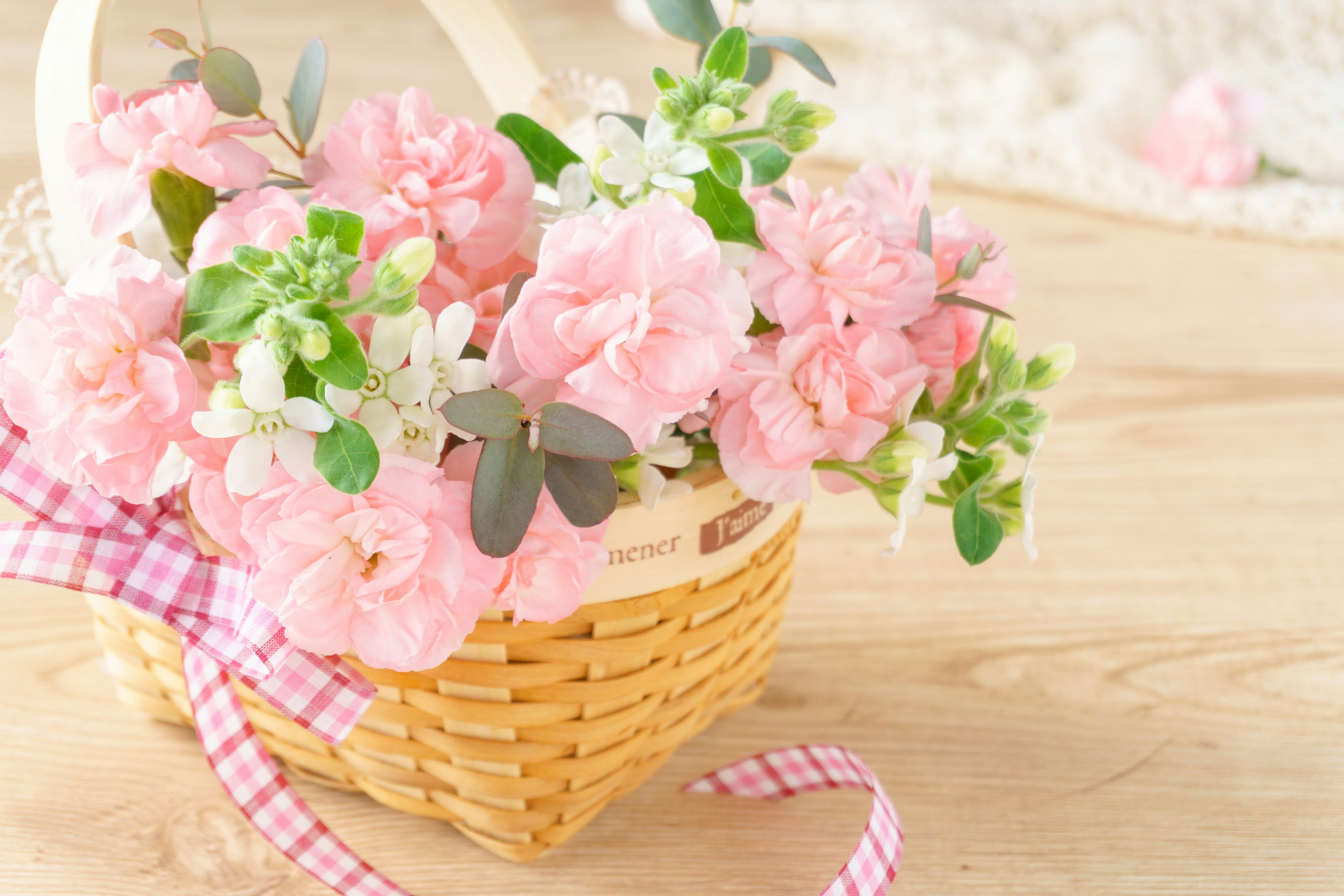 A basket filled with pink flowers and a checkered ribbon