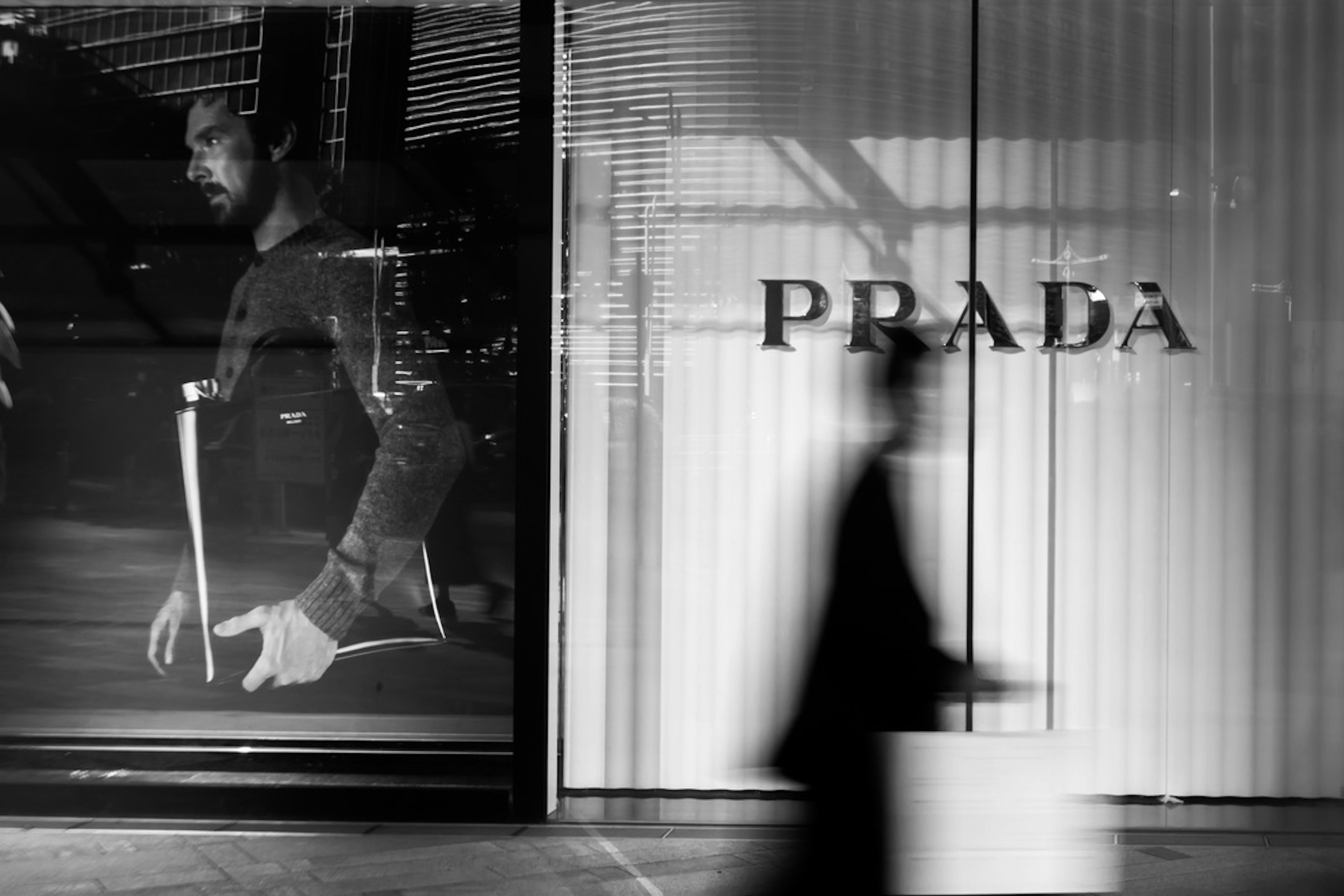 Silhouette of a person passing by a Prada store with a monochrome window display