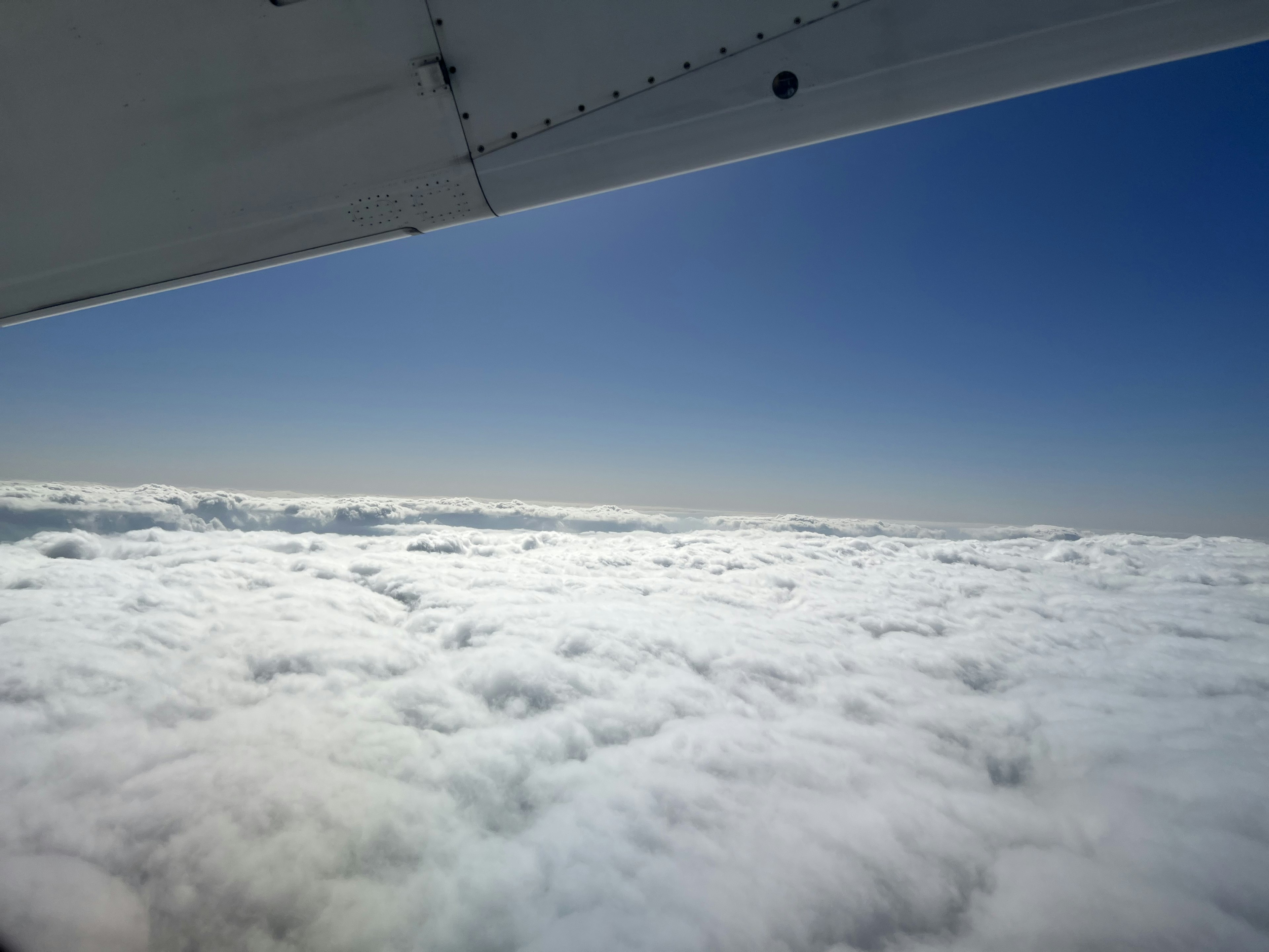 View from an airplane wing showing white clouds and a clear blue sky