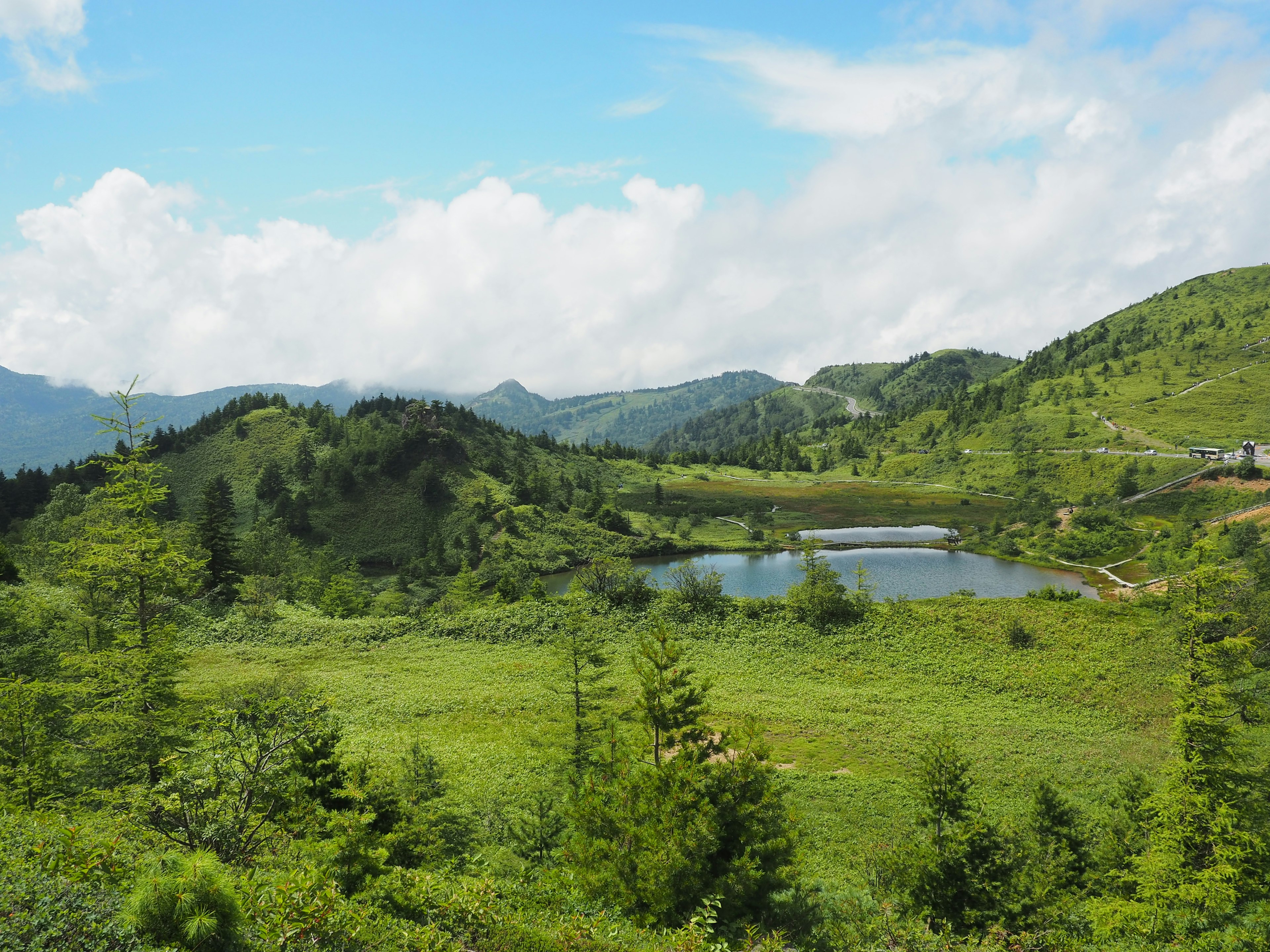 Beautiful landscape with blue sky and green hills featuring a pond and clouds