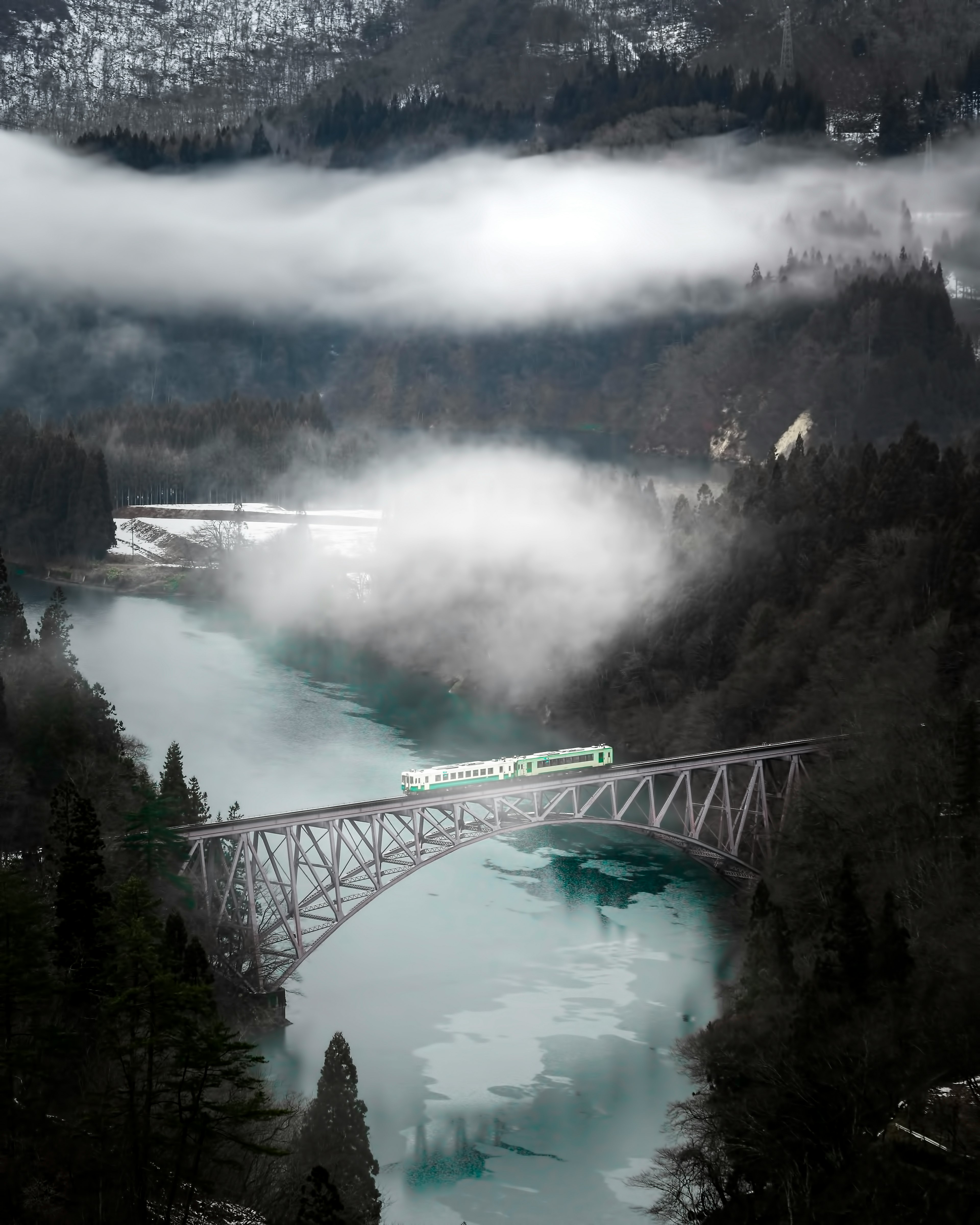 A scenic view of a train crossing a fog-covered river bridge