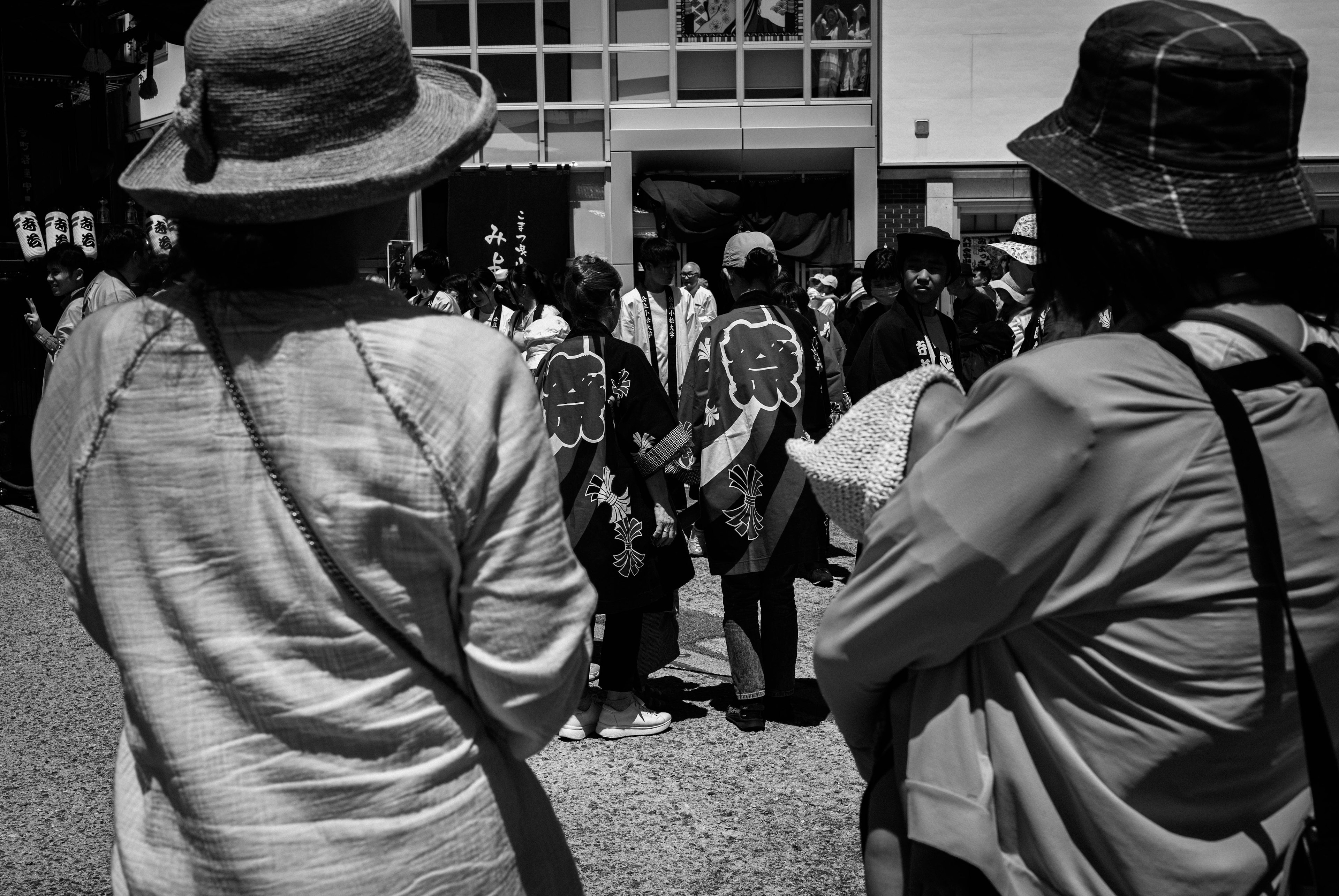 Due donne con cappelli che osservano un evento con una folla di persone sullo sfondo