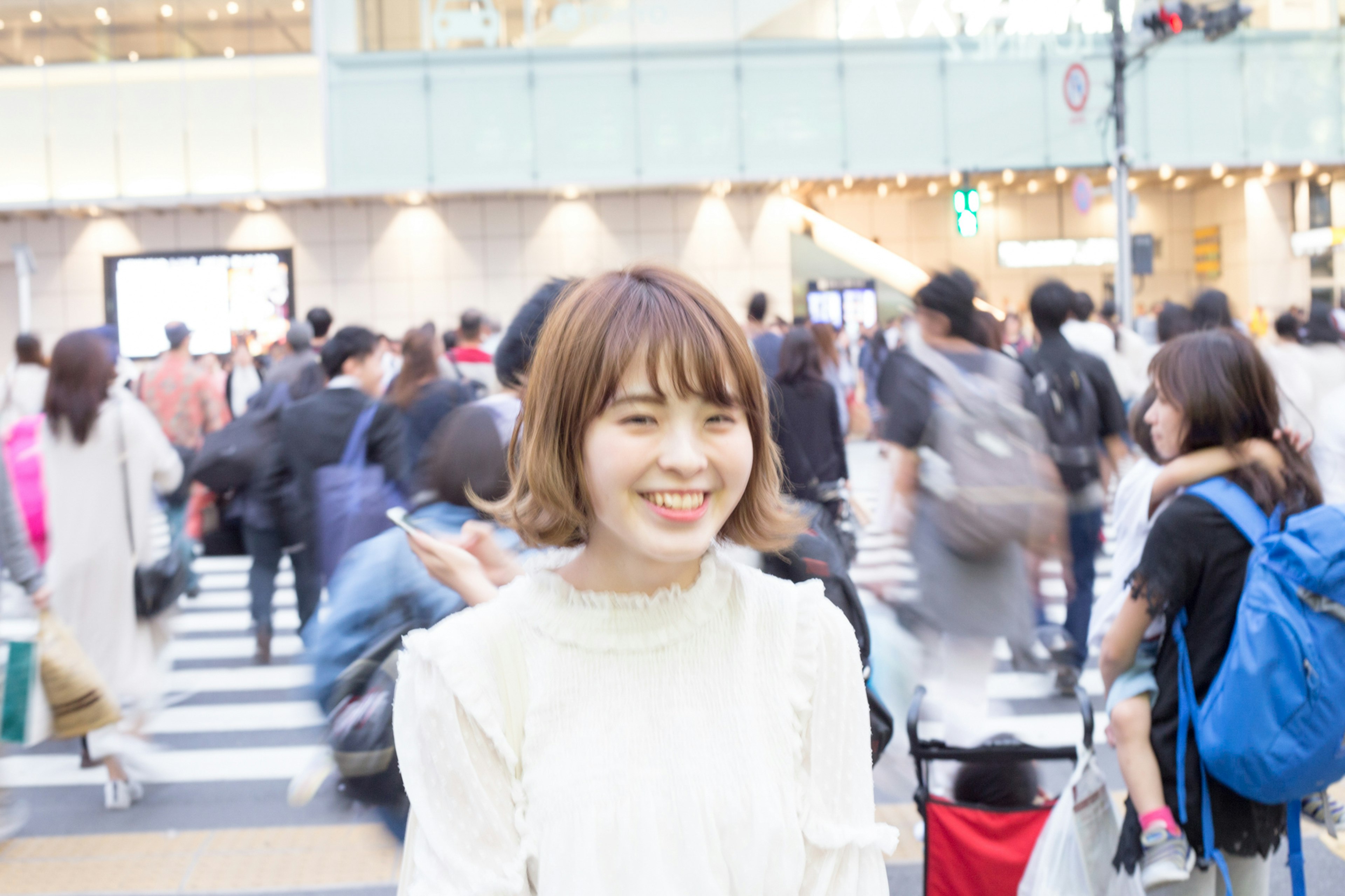 A smiling woman in the foreground at a busy crosswalk