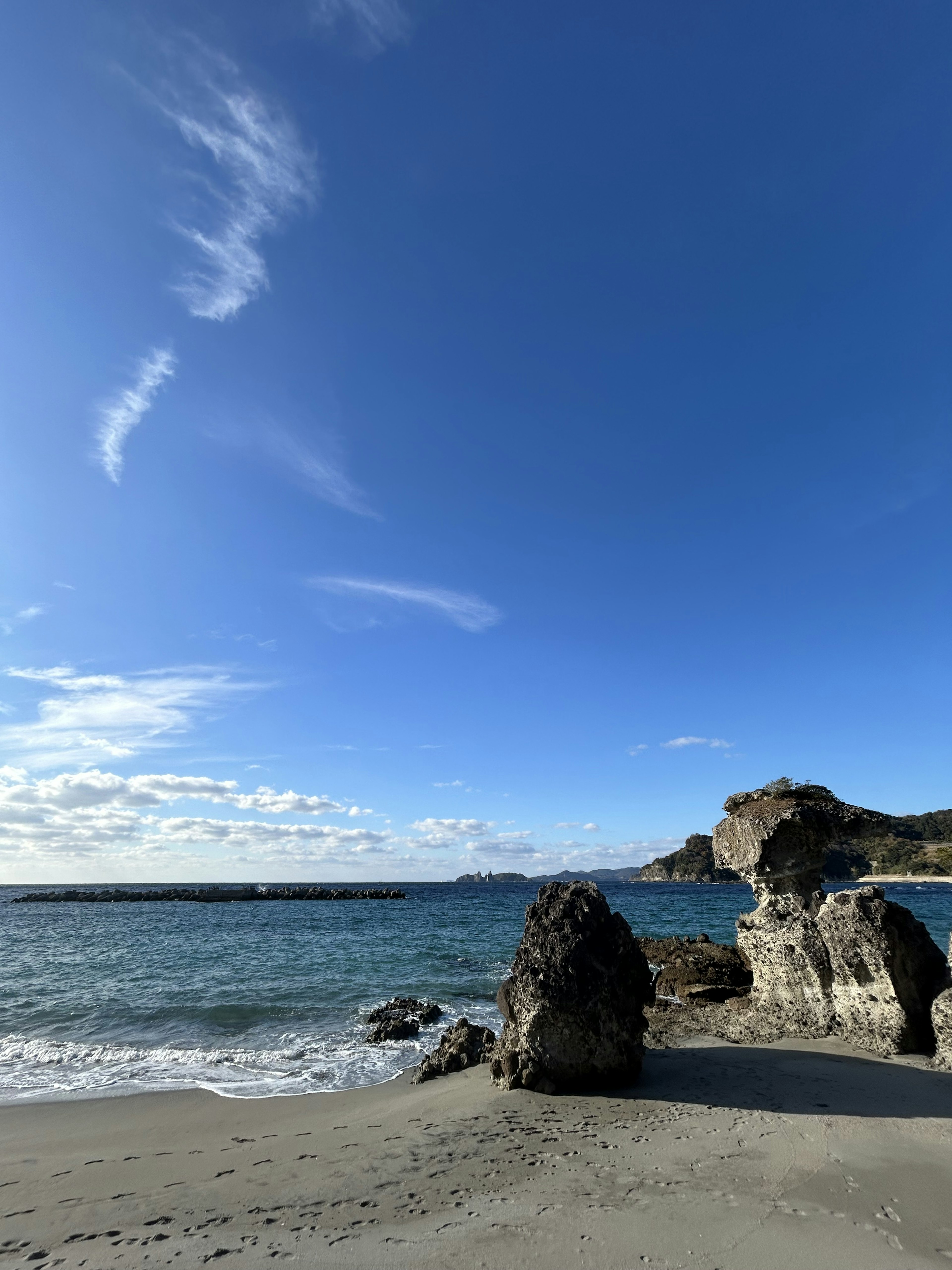 Coastal landscape with blue sky and white clouds featuring large rocks and calm sea