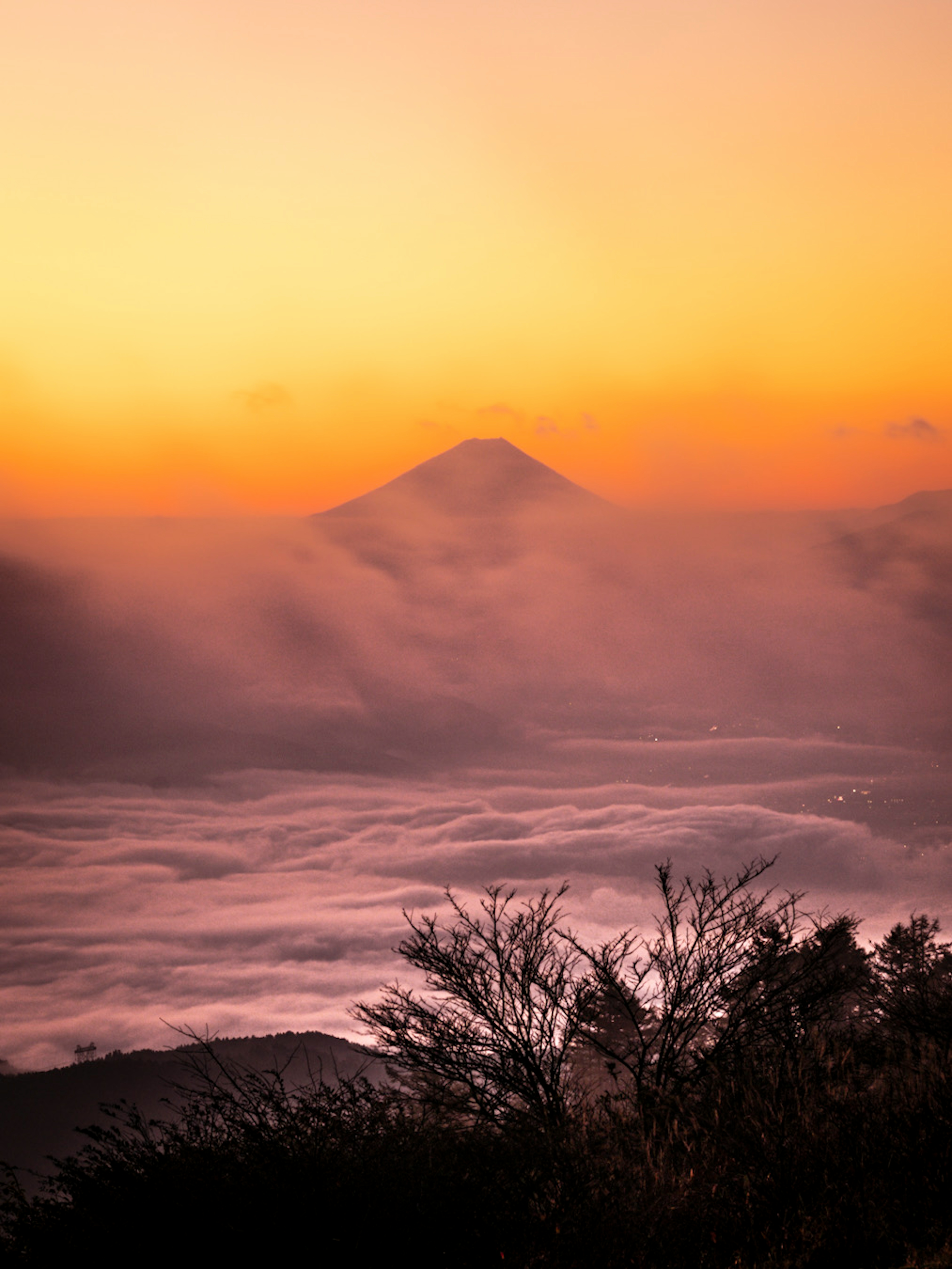 霧に包まれた山のシルエットとオレンジ色の夕焼け