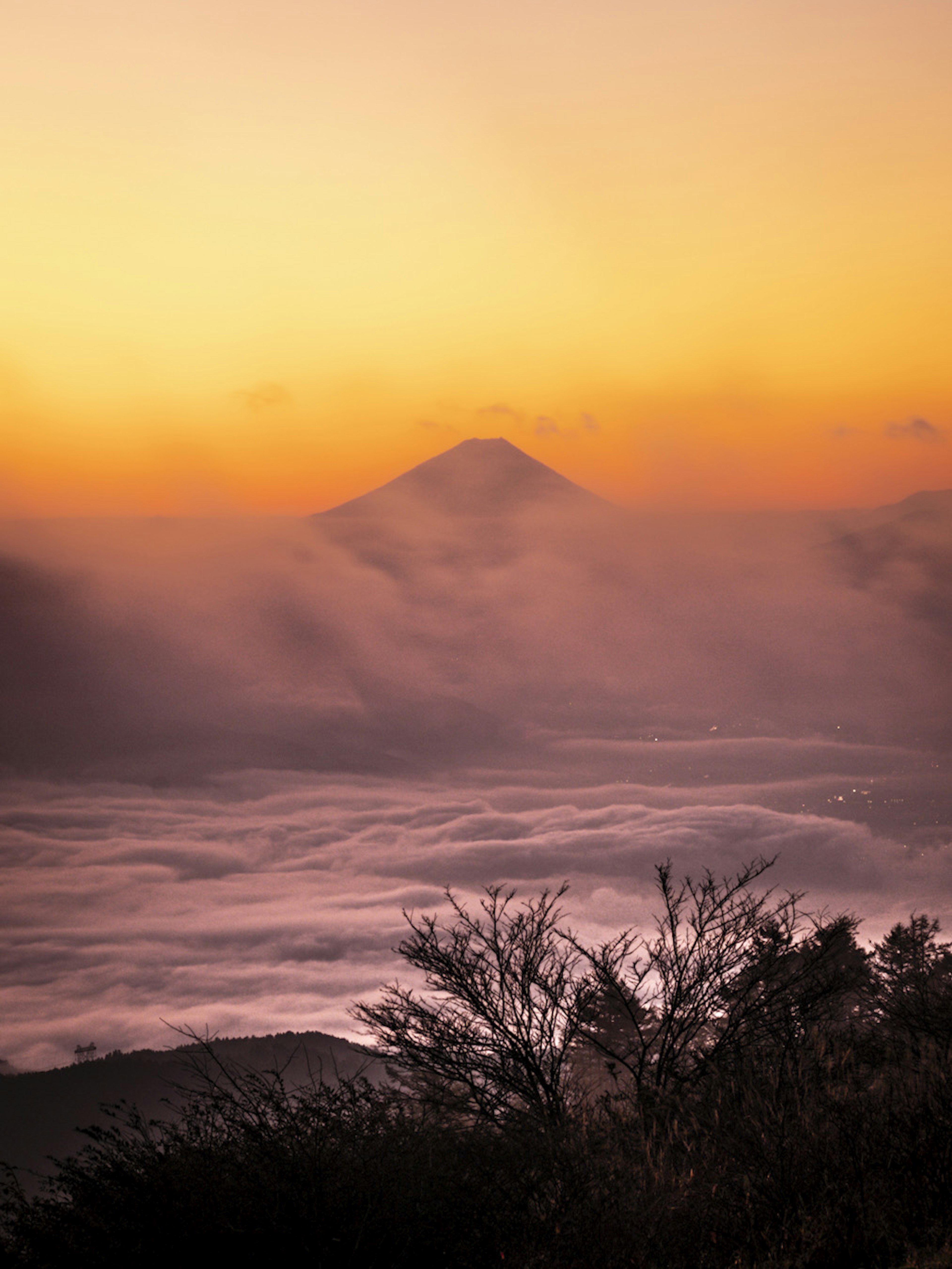 Silhouette di una montagna avvolta nella nebbia con un tramonto arancione