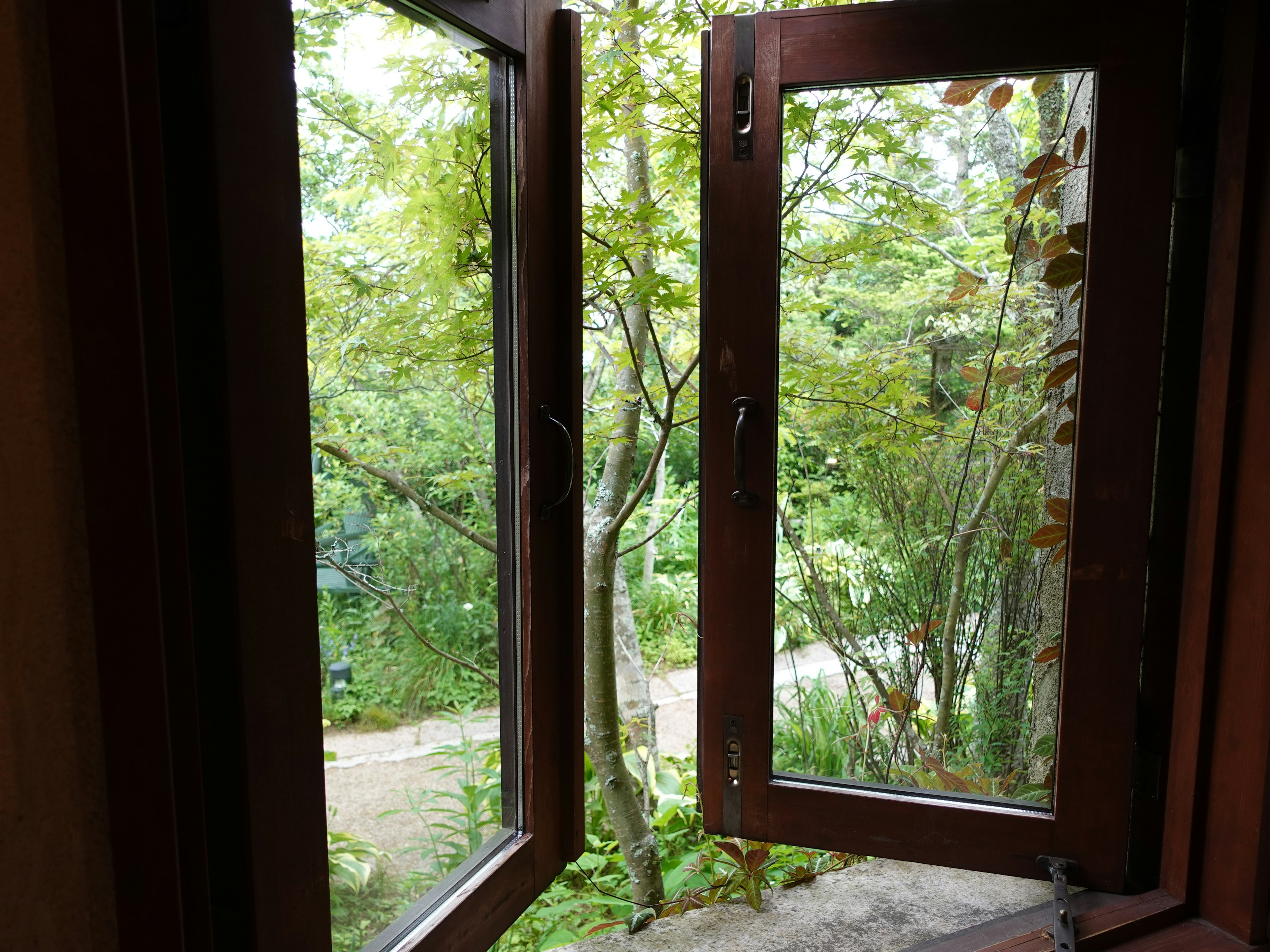 Holzfenster, das zu einer grünen Landschaft geöffnet ist