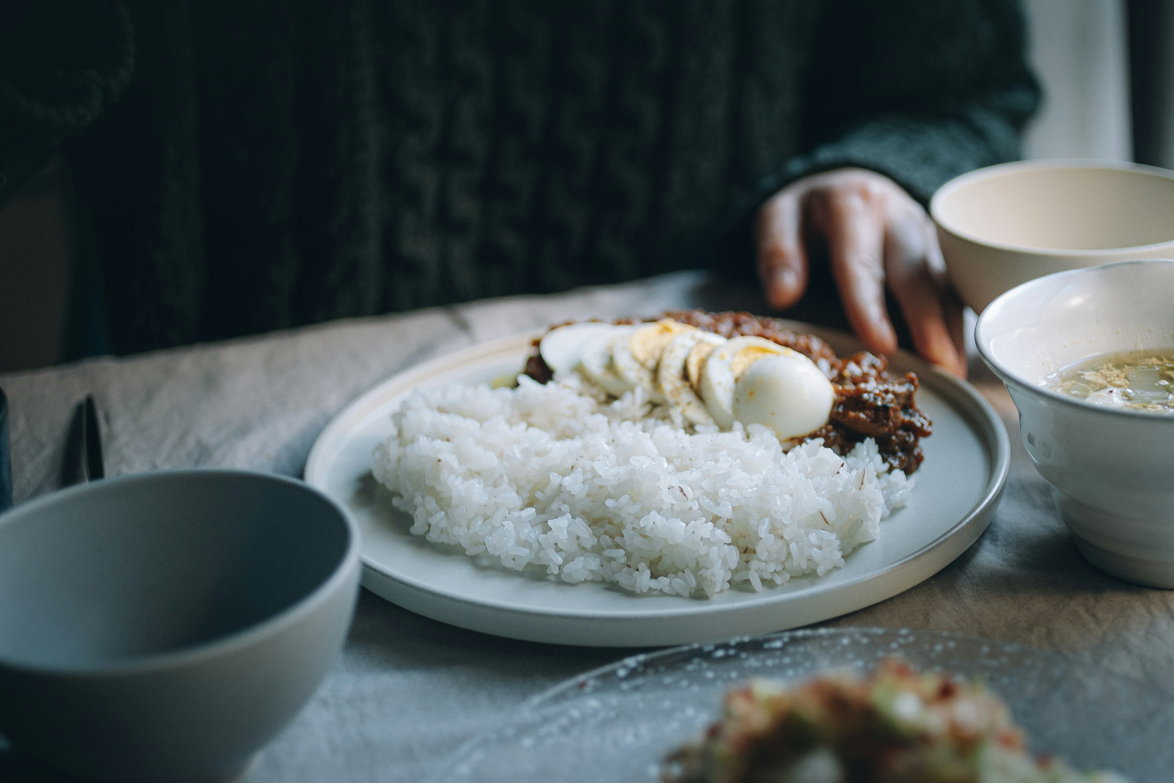 Piring dengan nasi putih dan hidangan daging di atas meja dengan tangan yang menjangkau piring