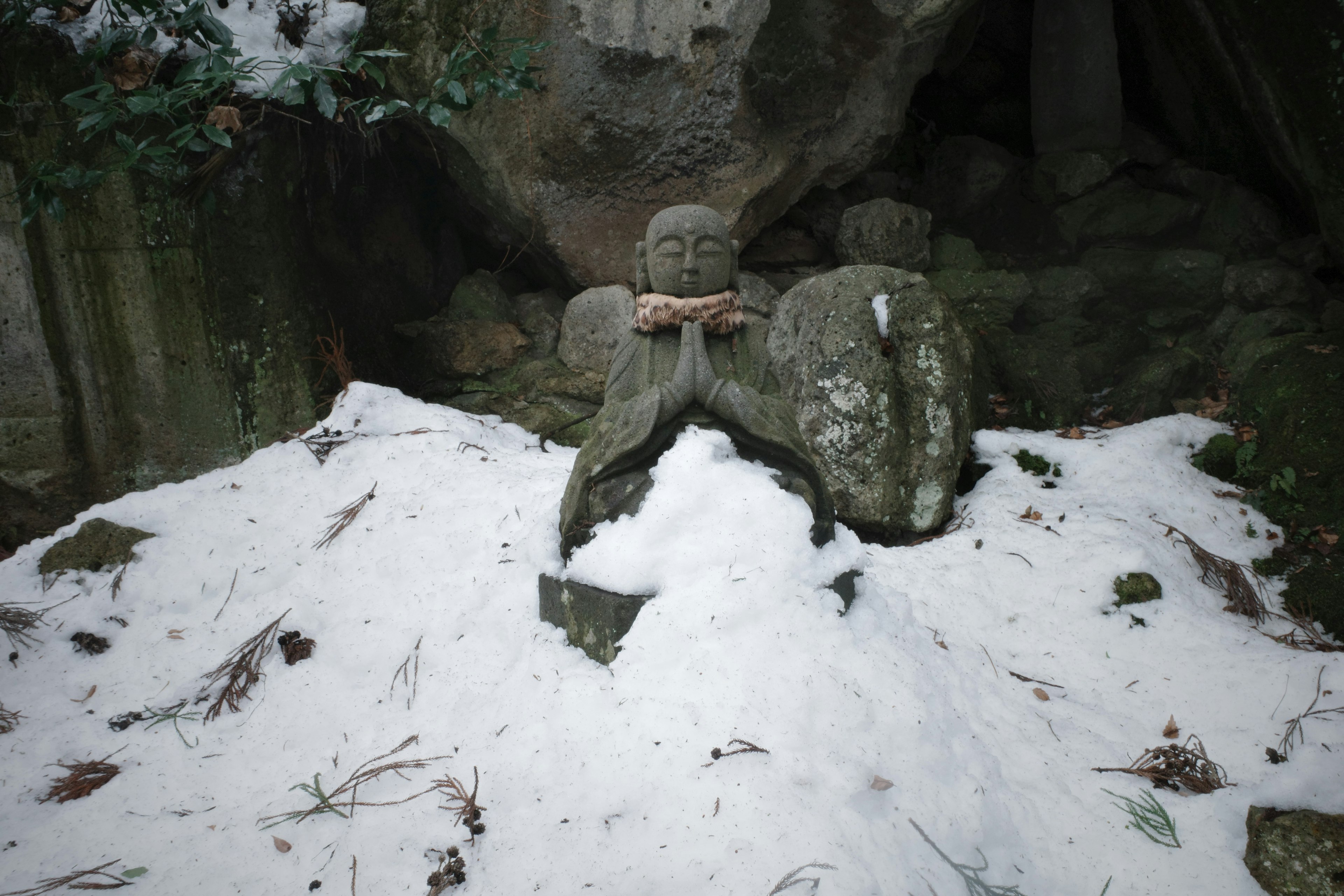 一座被雪覆蓋的石佛像，四周環繞著岩石