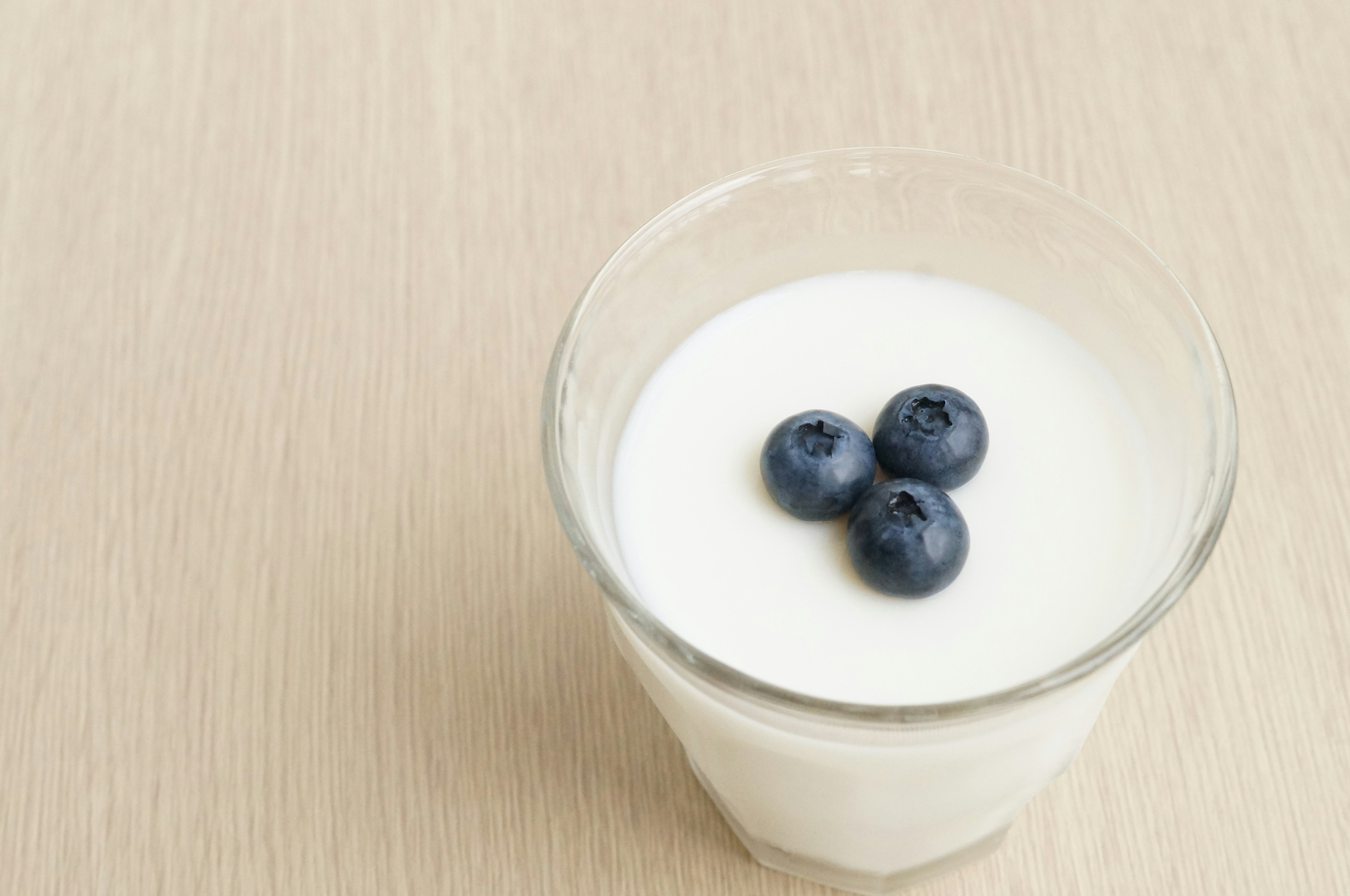 A clear glass of yogurt topped with three blueberries