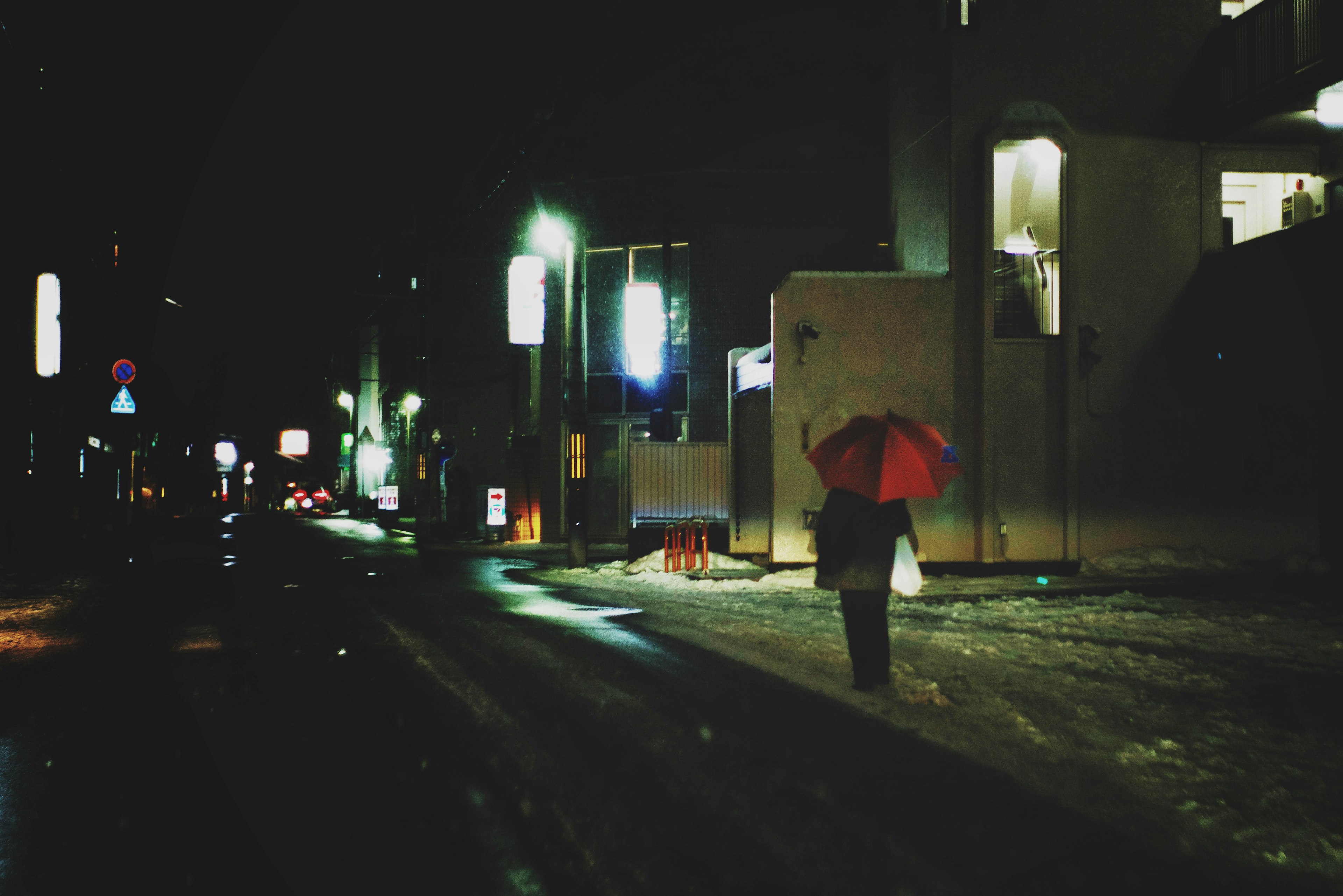 Person walking in the night with a red umbrella