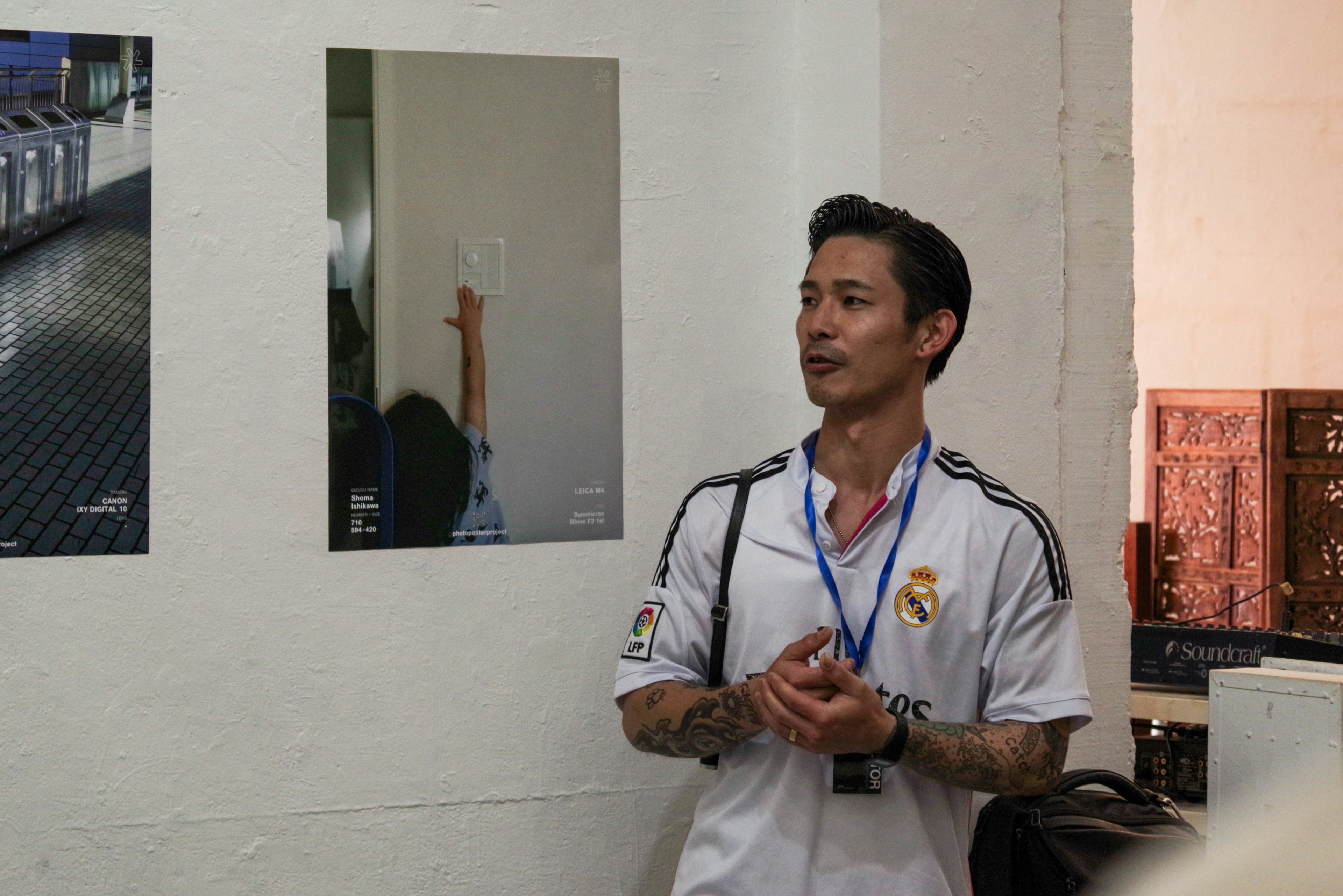 A man speaking at an exhibition with photographs displayed in the background