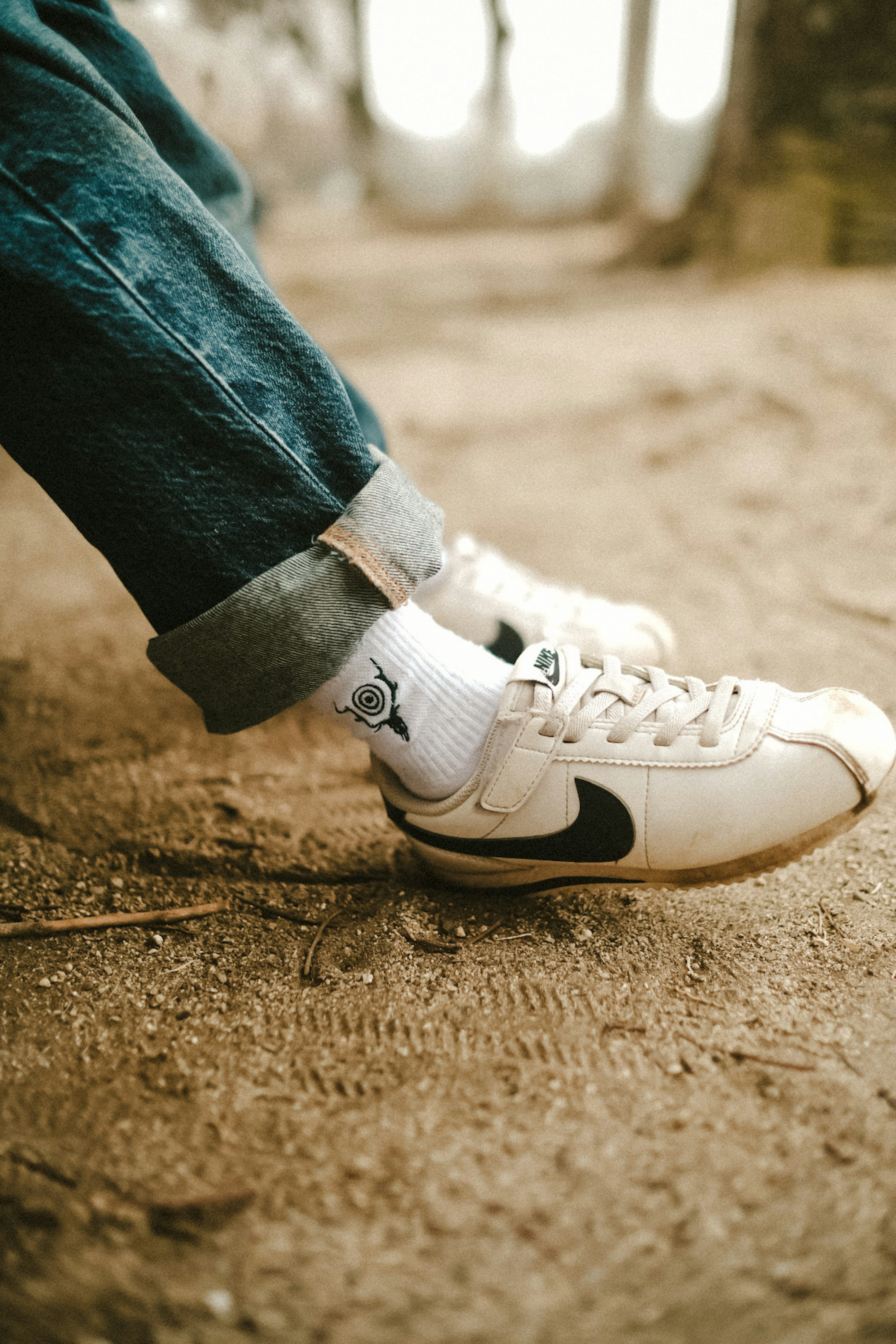 Close-up of a person's feet wearing white Nike sneakers and rolled denim jeans