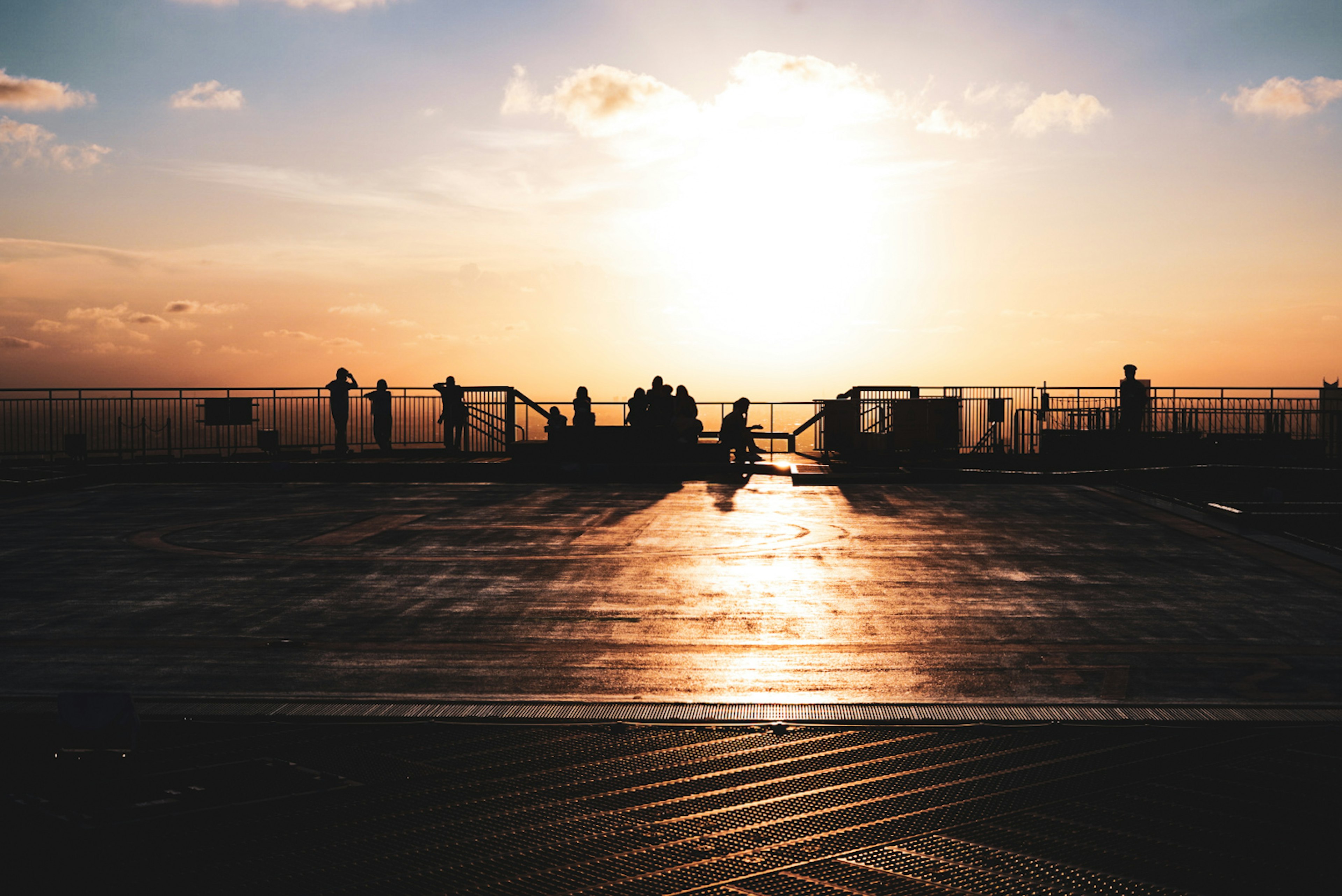 夕日を背にした人々が並ぶ海辺の風景