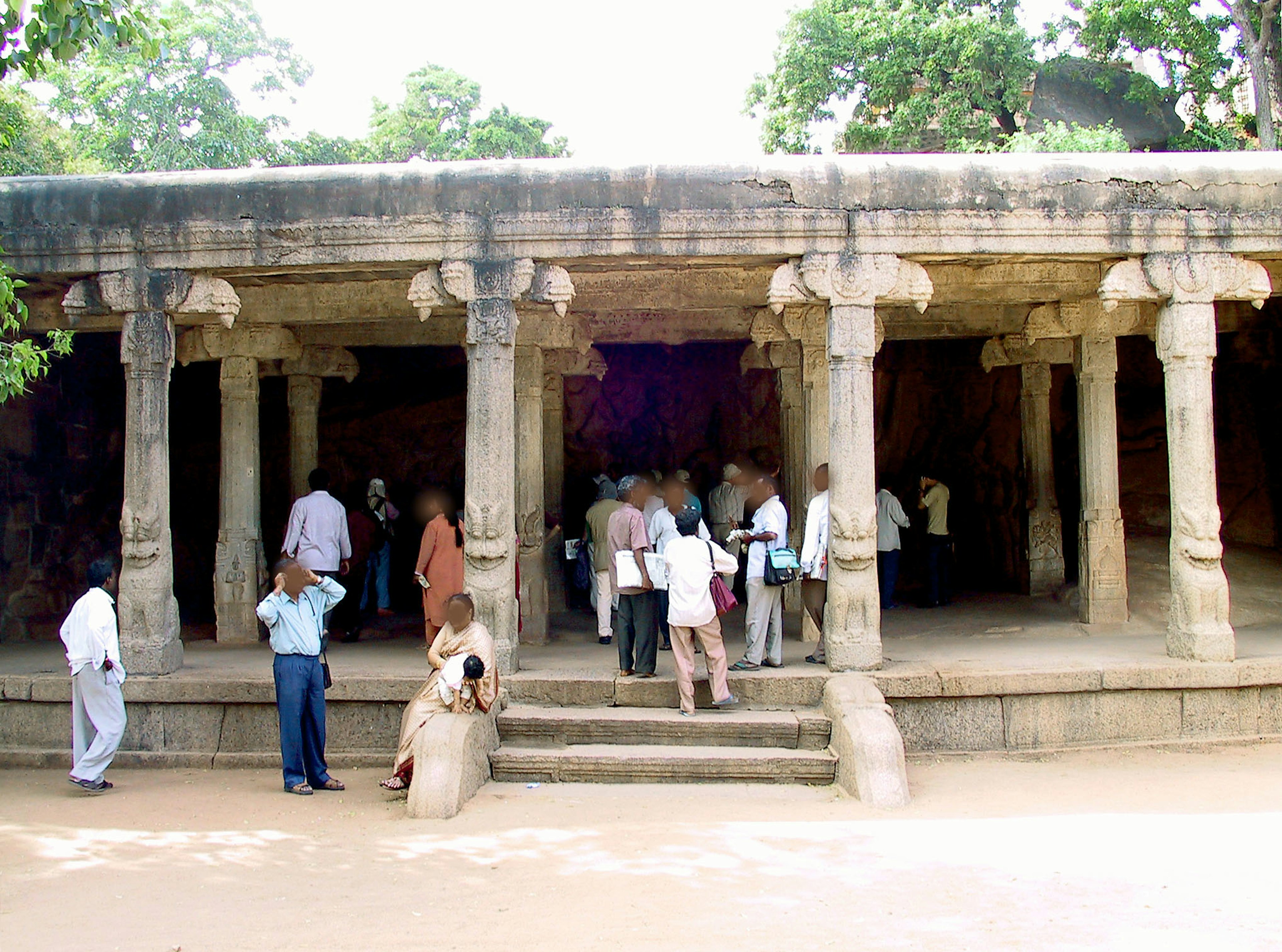 Exterior de un antiguo templo de piedra con columnas y escalones visibles turistas explorando la zona